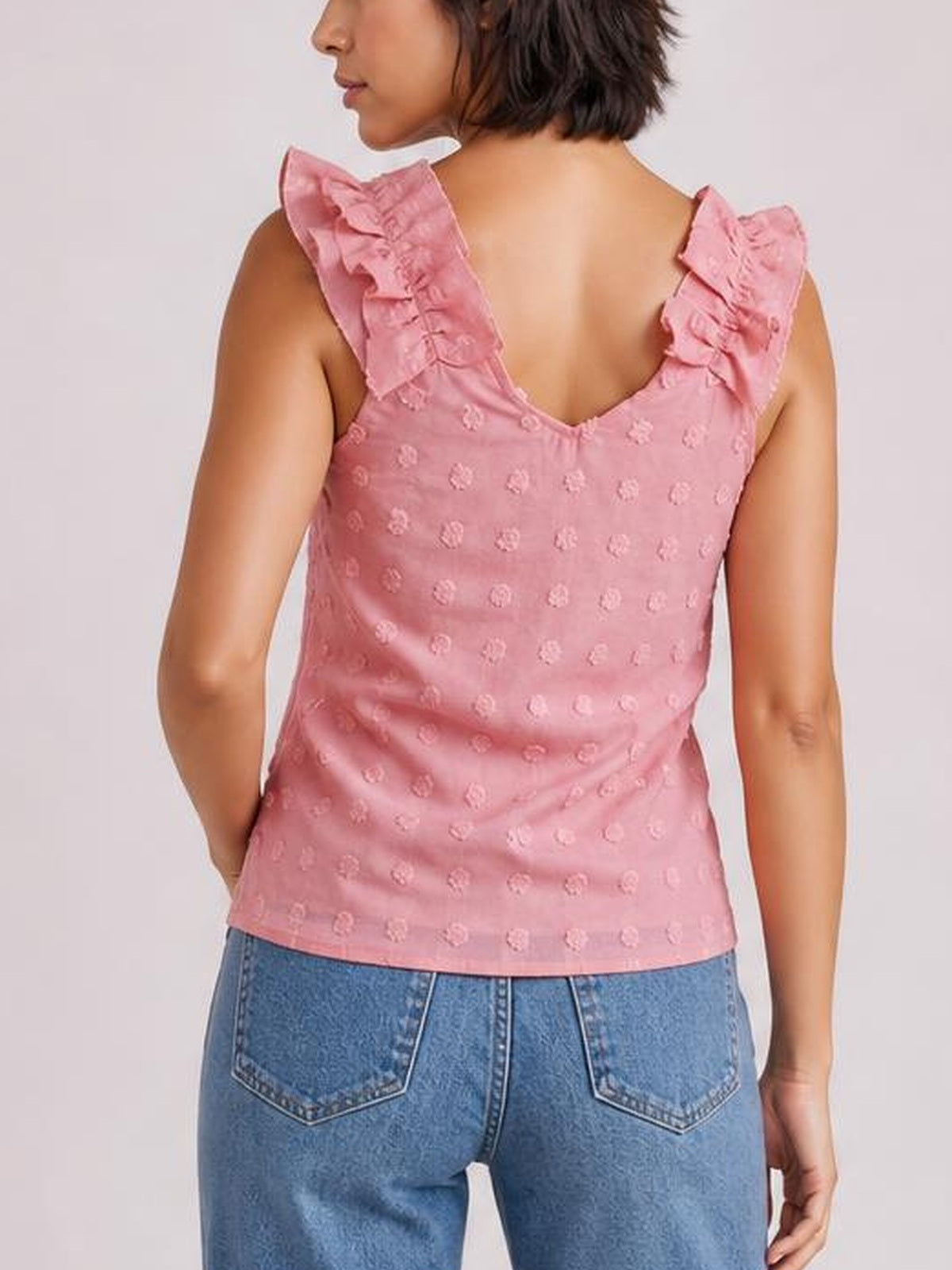 A model turned away wears a pink Swiss dot tank with a V-shaped back, ruffled shoulder straps, and a fitted straight silhouette.