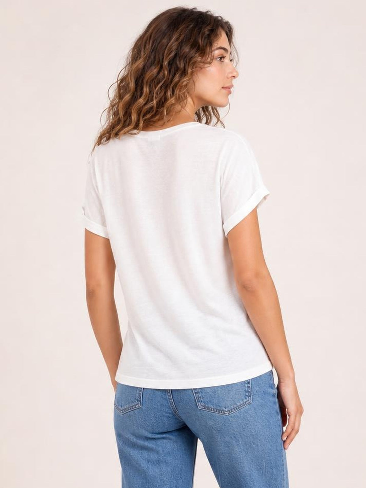 A model poses in a back three-quarter view wearing a white round neck short sleeve T-shirt with rolled cuffs and a relaxed straight silhouette.