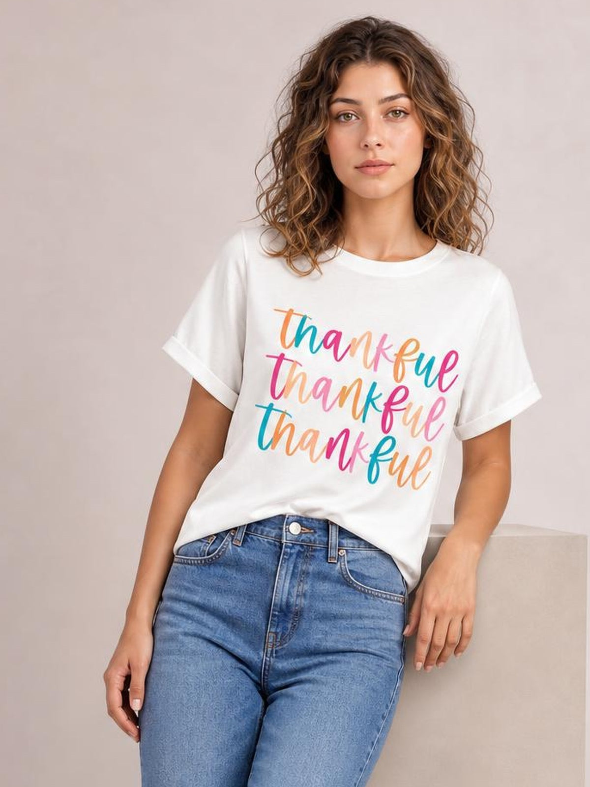 Model wears a white THANKFUL round neck short sleeve T-shirt with rolled cuffs and colorful stacked lettering in a relaxed silhouette.
