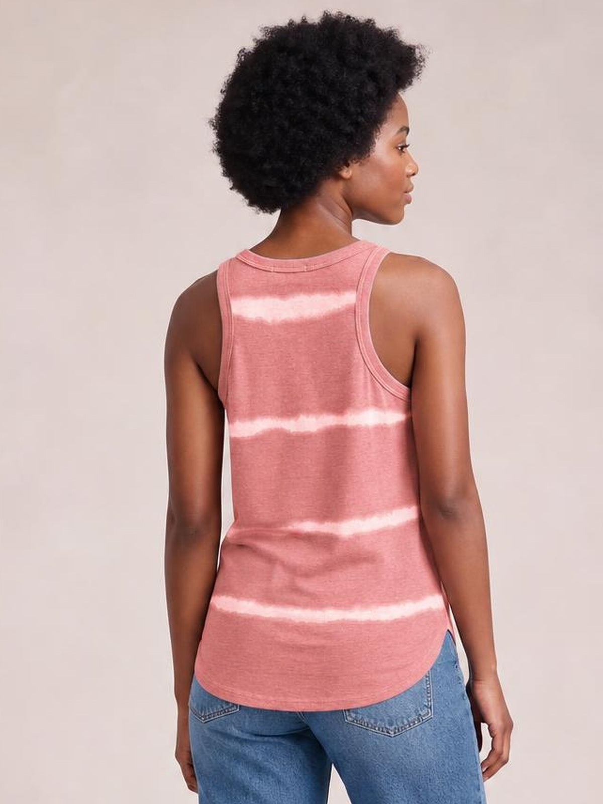 Model shown from the back wearing a pink tie-dye round neck tank with wide shoulder straps, contrast horizontal bands, and a relaxed curved-hem silhouette.