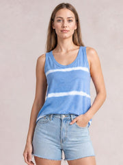 Model poses in a blue tie-dye round neck tank with a relaxed silhouette, wide shoulder straps, and horizontal white bands, one hand in her shorts pocket.