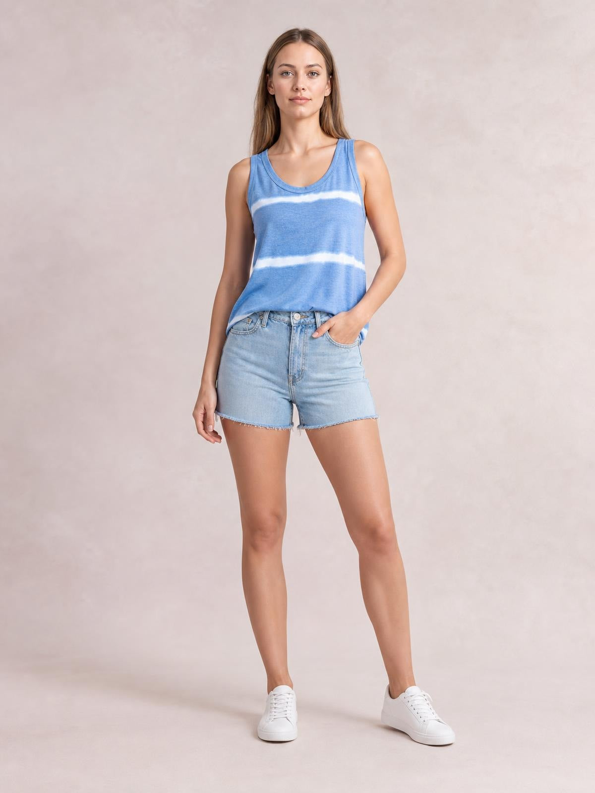 Model wearing a blue tie-dye round neck tank with wide shoulder straps and a relaxed straight silhouette, posing with one hand in her shorts pocket.