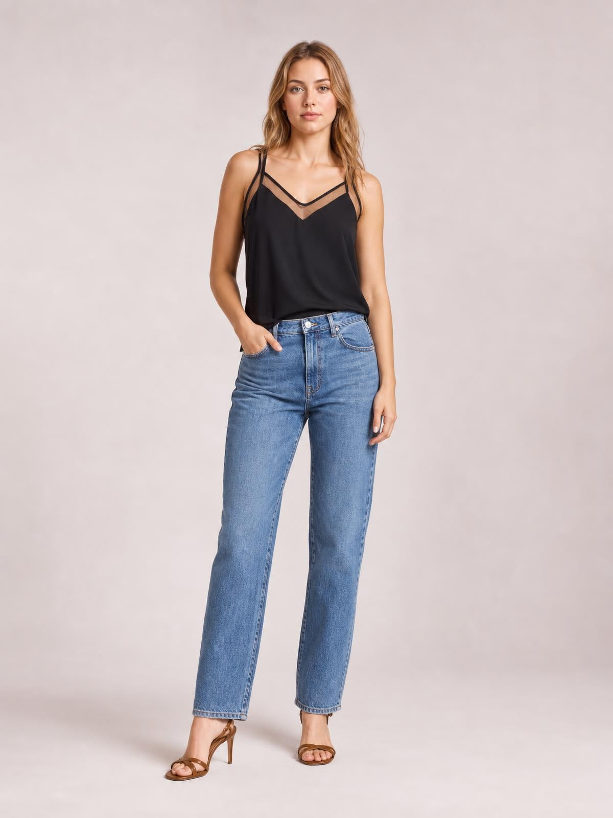 Model poses in a black V-neck spaghetti strap cami with semi-sheer trim and a relaxed silhouette, paired with jeans.
