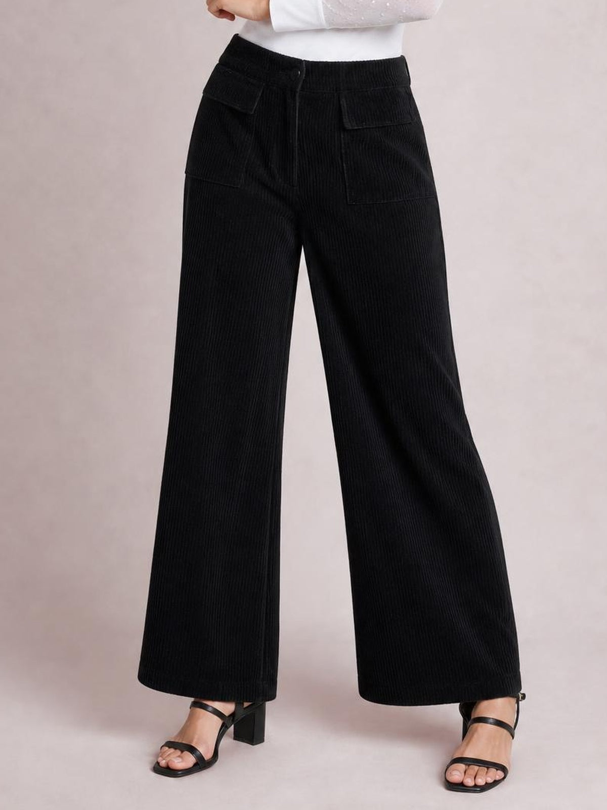 A model wears black wide-leg corduroy pants with a high-rise waistband, button closure, multiple patch pockets, and straight flowing legs.