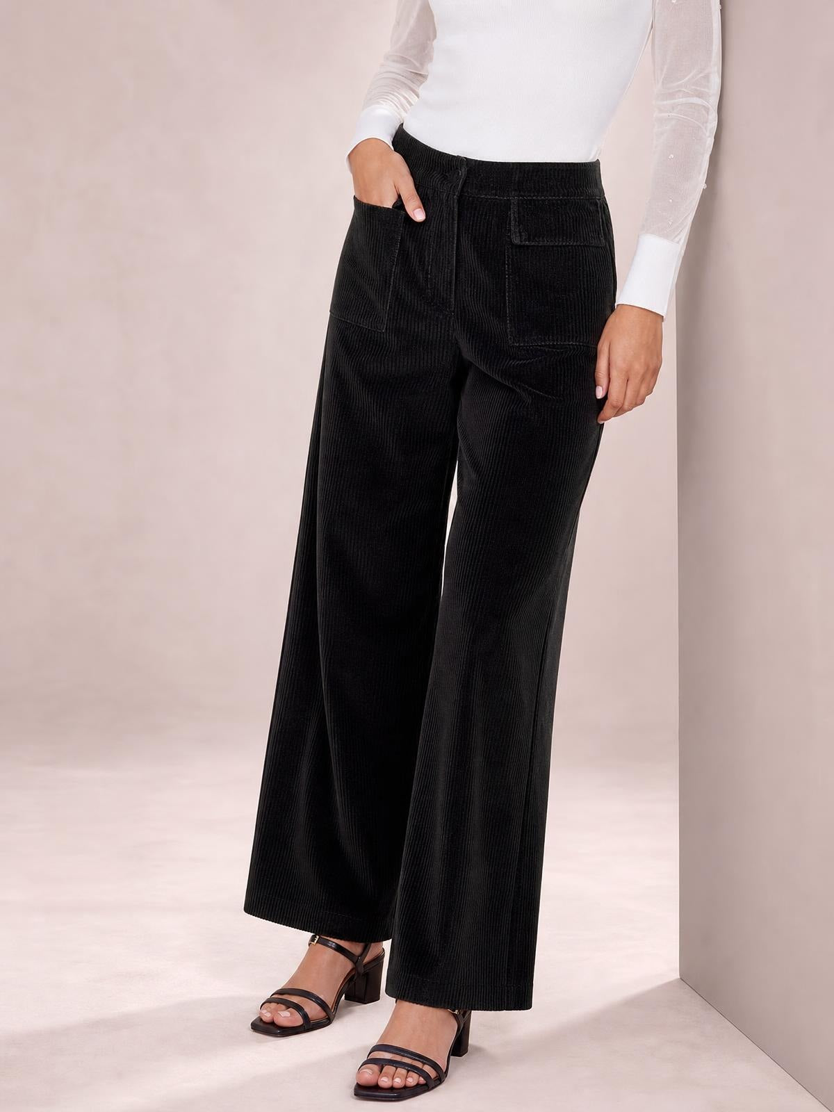 A model stands in black wide-leg corduroy pants with ribbed texture, a comfortable waistband, front pockets, and a relaxed full-length silhouette.