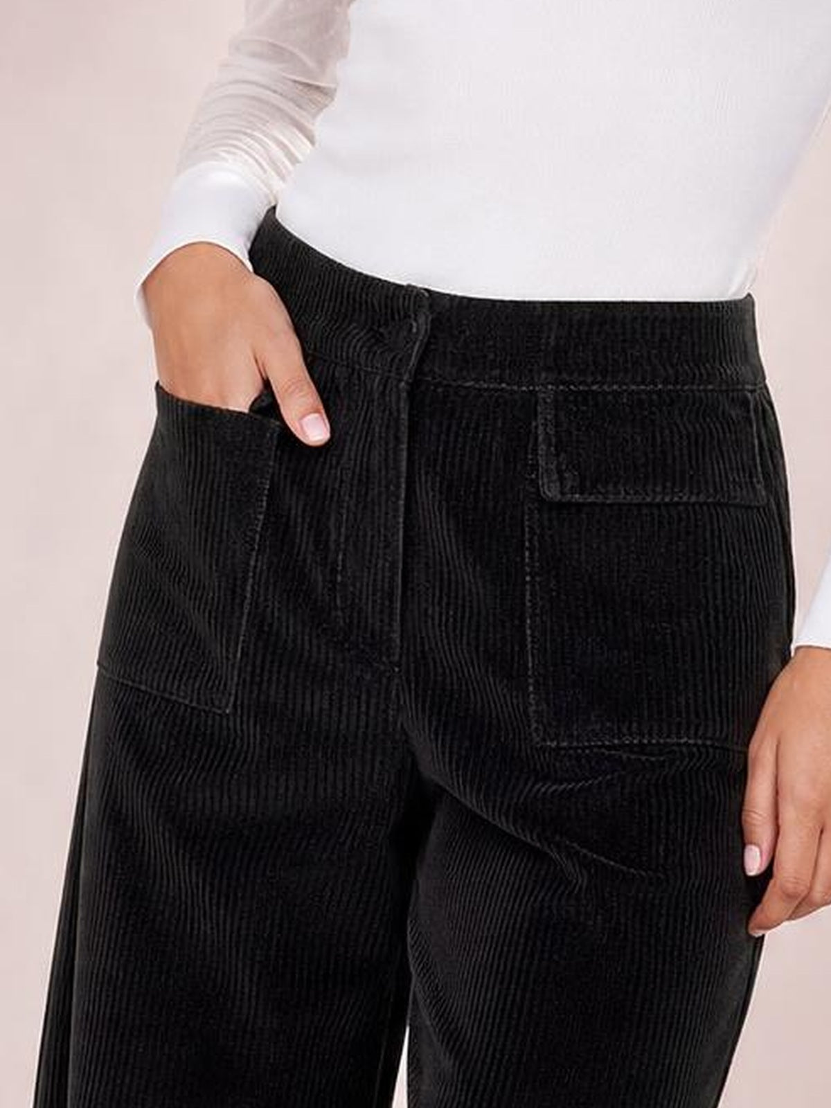 Model wears black wide-leg corduroy pants with a high-rise waistband, roomy silhouette, front pockets, and utility-style patch pockets.