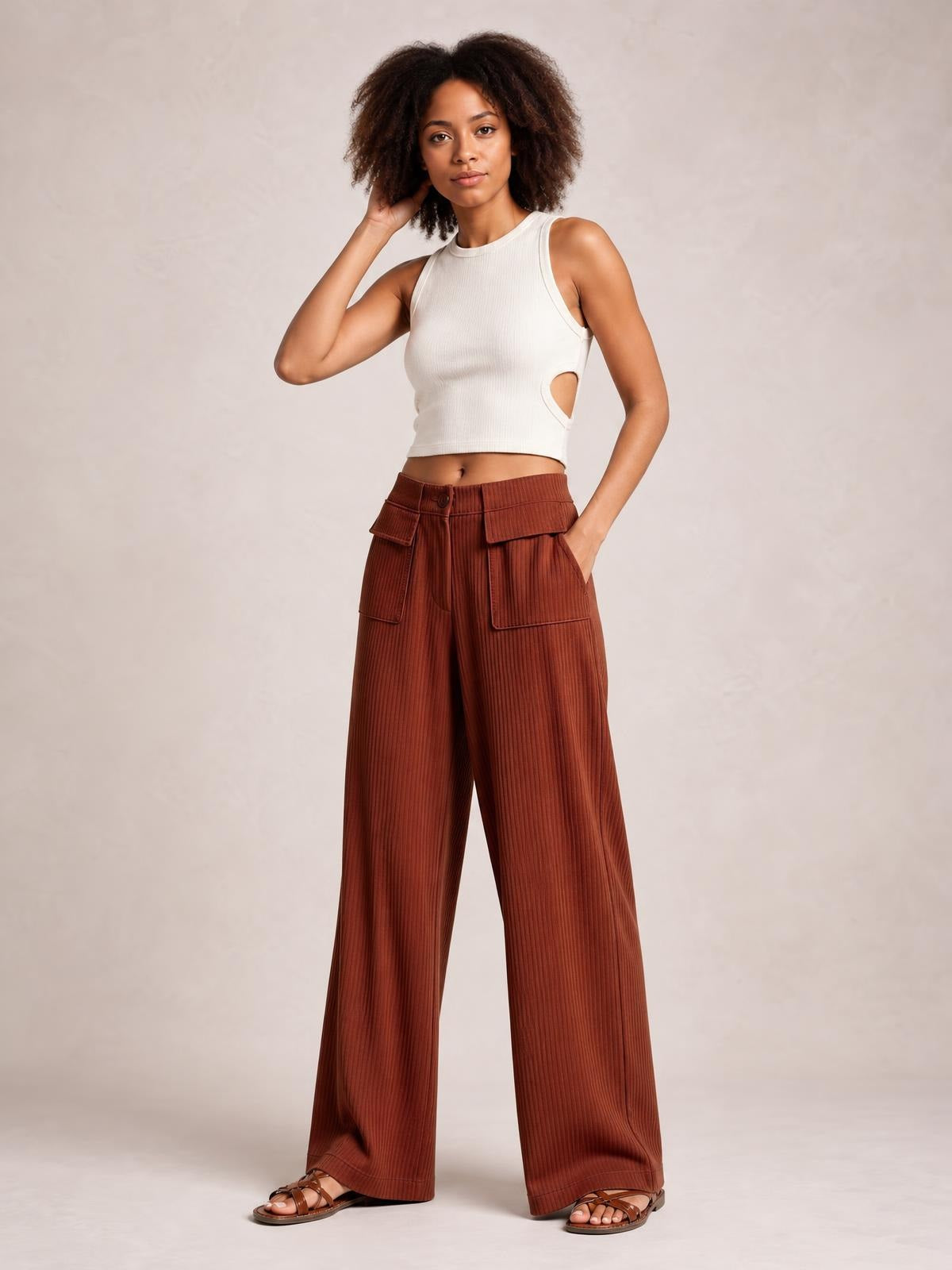 Model poses in rust-brown wide-leg corduroy pants with vertical ribbing, a buttoned waistband, and large front patch pockets.