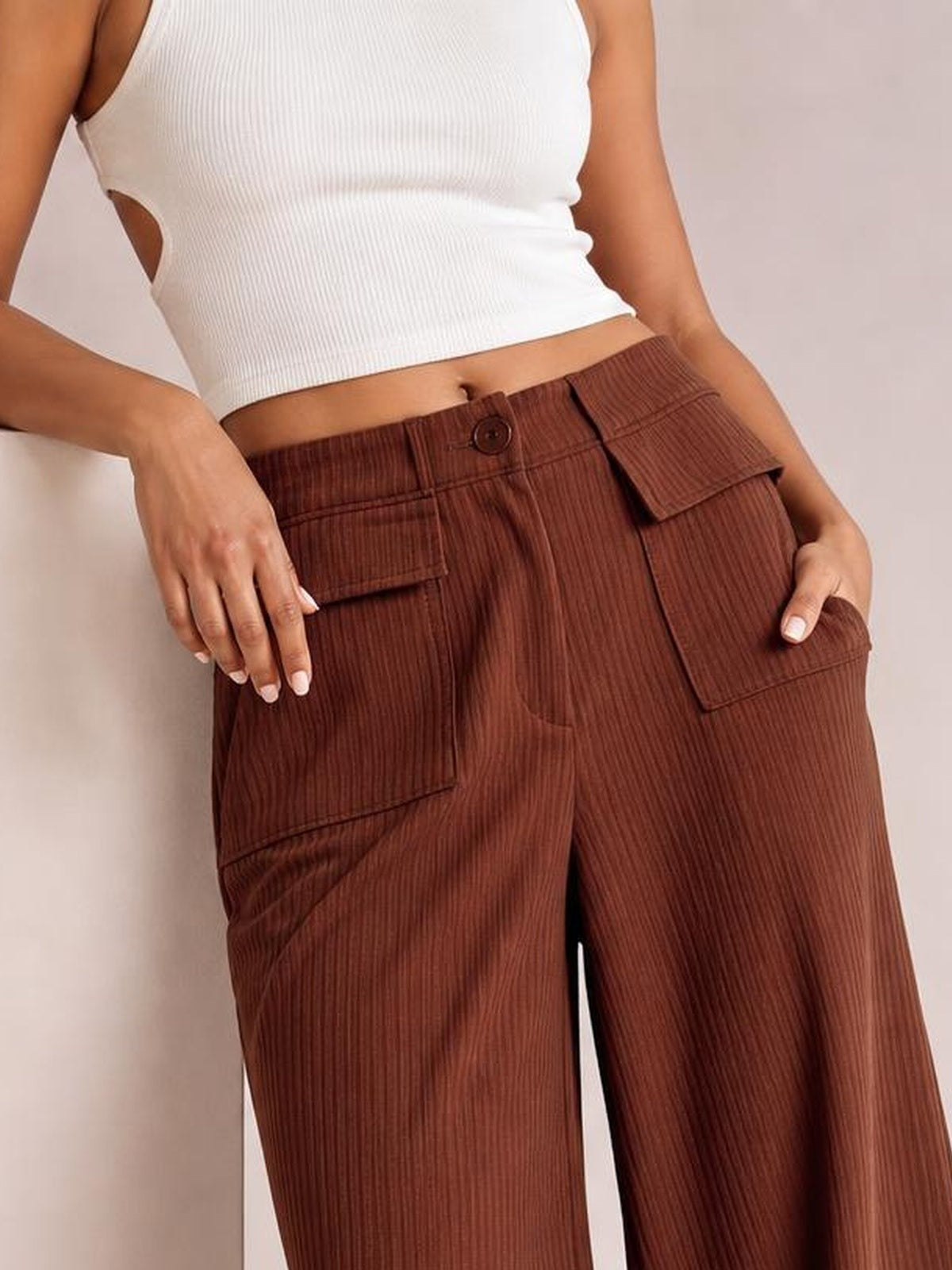 Model poses with hands at the hips, wearing brown corduroy wide-leg pants with a button waistband and multiple flap pockets.