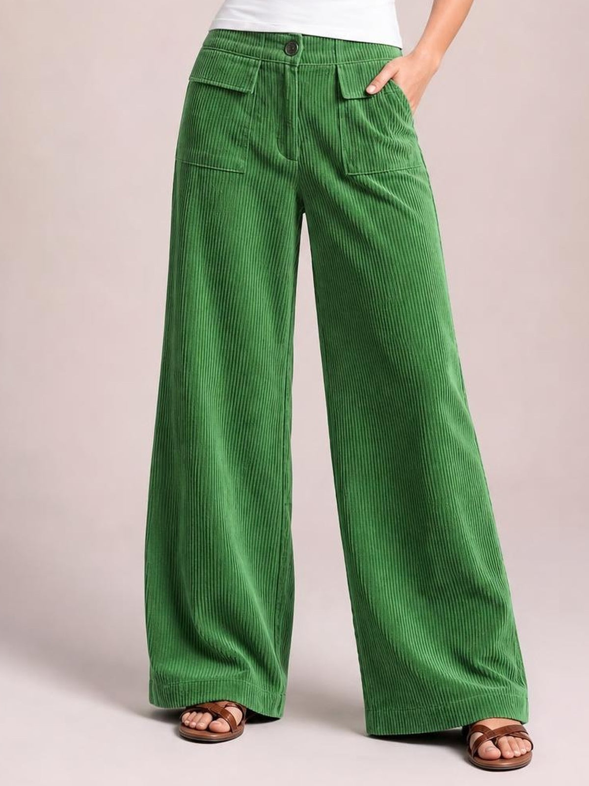 A model stands in green wide-leg corduroy pants with a button closure, zip fly, and multiple flap pockets, showing a relaxed, flowing silhouette.