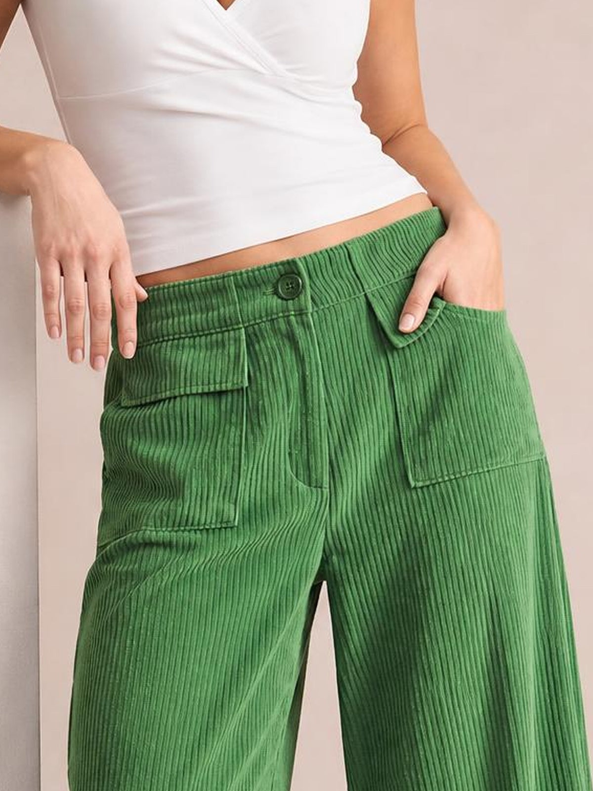 Model poses with hands at the waist, highlighting bright green wide-leg corduroy pants with a button closure, ribbed texture, and multiple patch pockets.
