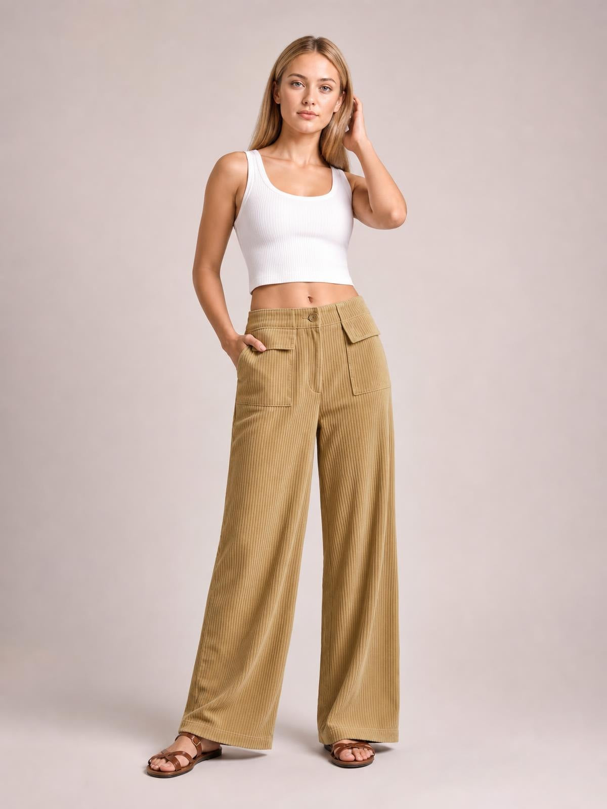 A model poses with one hand in the pocket, wearing tan wide-leg corduroy pants with a button waistband, ribbed texture, and roomy cargo-style pockets.