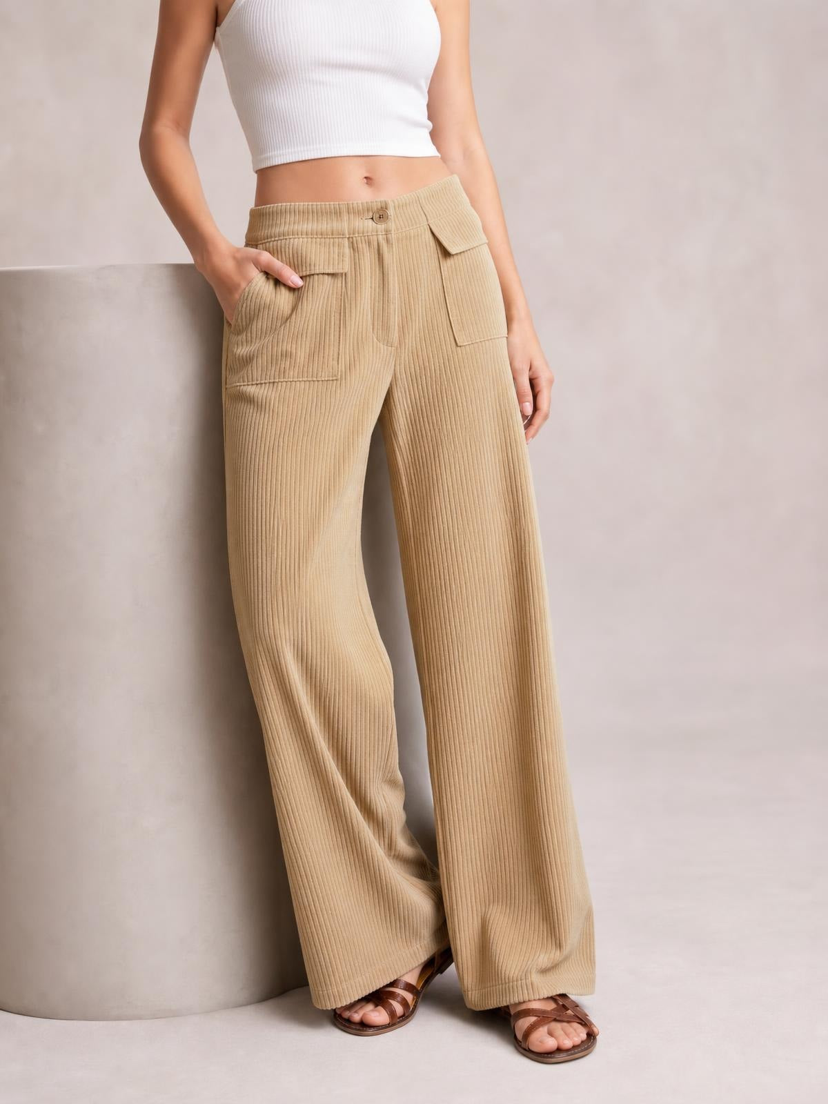 Model leans against a surface wearing tan wide-leg corduroy pants with a high-rise waistband, button closure, and multiple flap pockets.