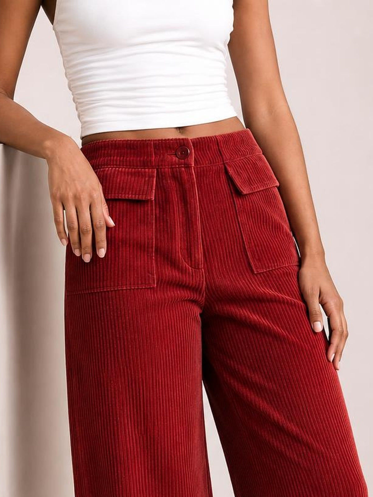 Model poses with one hand on her hip wearing red wide-leg corduroy pants with a button waistband, textured vertical ribs, and multiple patch pockets.
