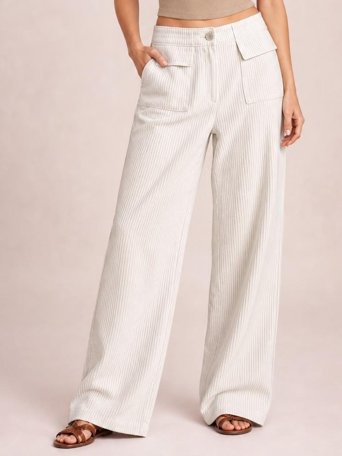Model wears white wide-leg corduroy pants with a button closure, vertical ribbed texture, and large flap pockets, posing with one hand in a pocket.