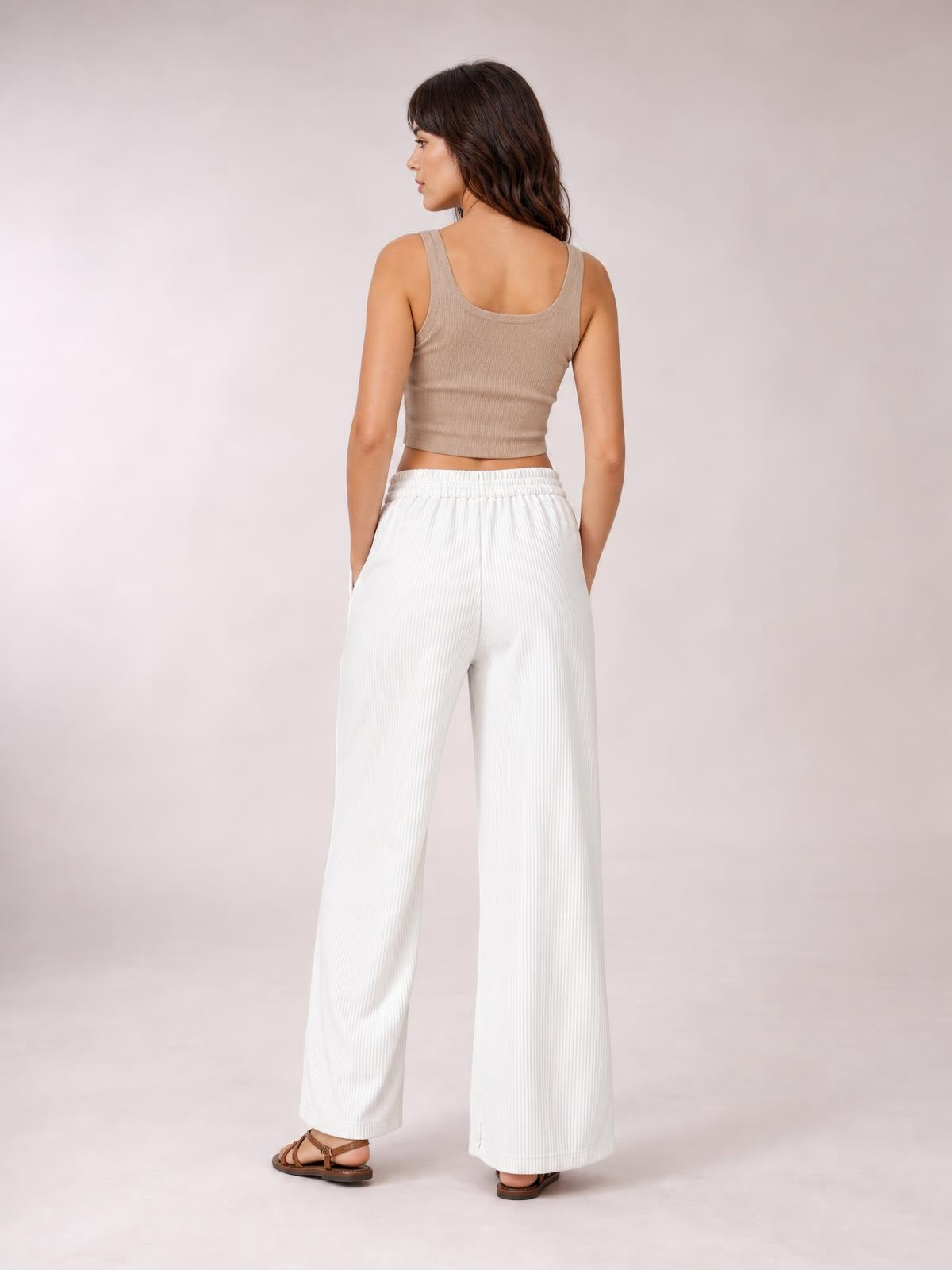 A model poses from behind in white wide-leg corduroy pants with a comfortable elastic waistband, vertical ribbed texture, and side pockets.