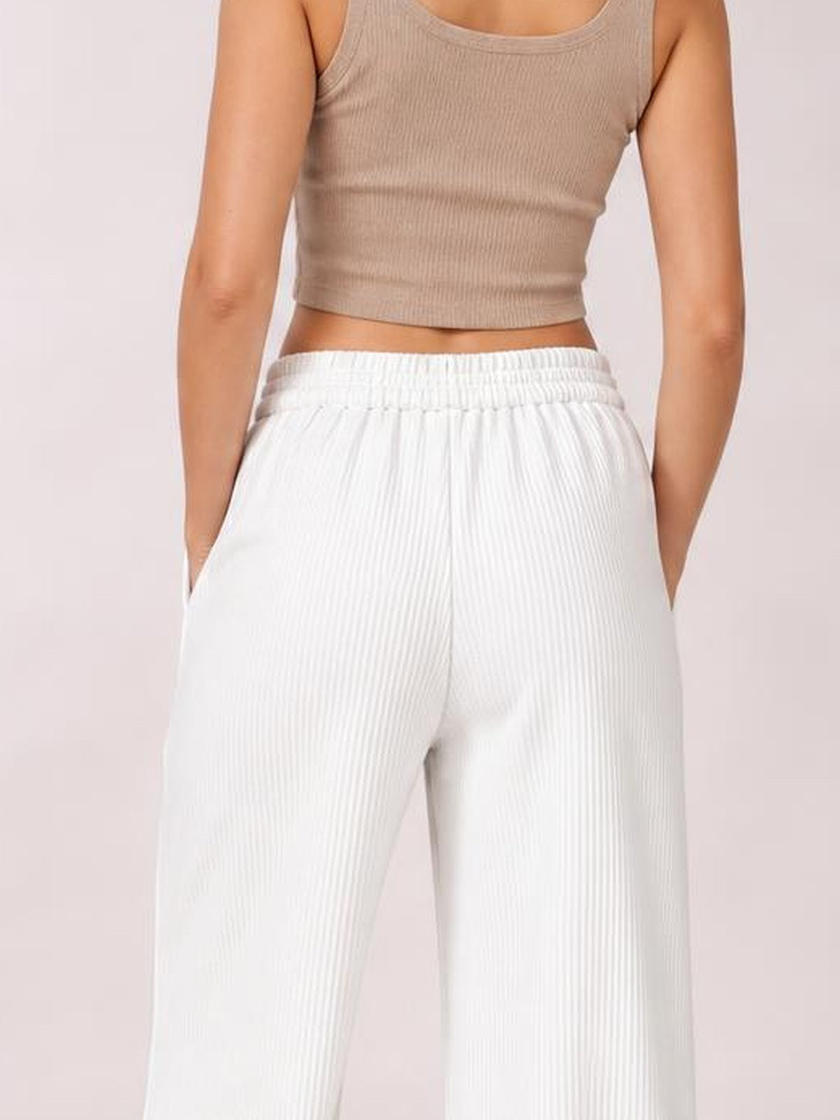 A model wears white wide-leg corduroy pants with a gathered elastic waistband and side pockets, standing with both hands tucked into the pockets.