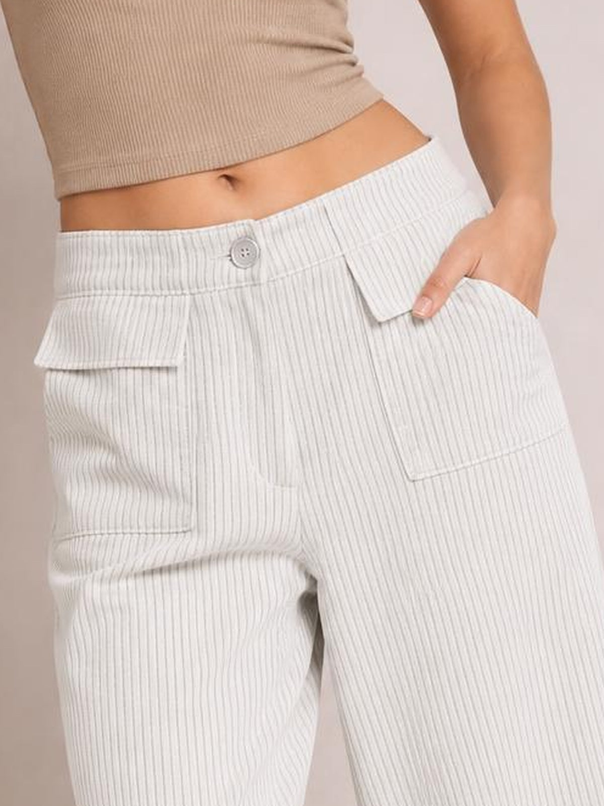A model wears light gray wide-leg corduroy pants with a buttoned waistband, vertical ribbed texture, and roomy patch pockets while posing with one hand tucked inside.