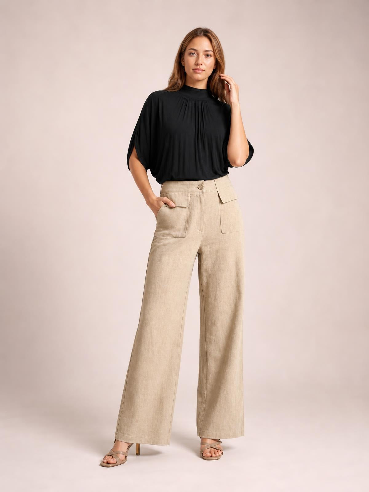 Model poses with one hand in the pocket, wearing beige wide leg pants with a high waist, button closure, and large front patch pockets.