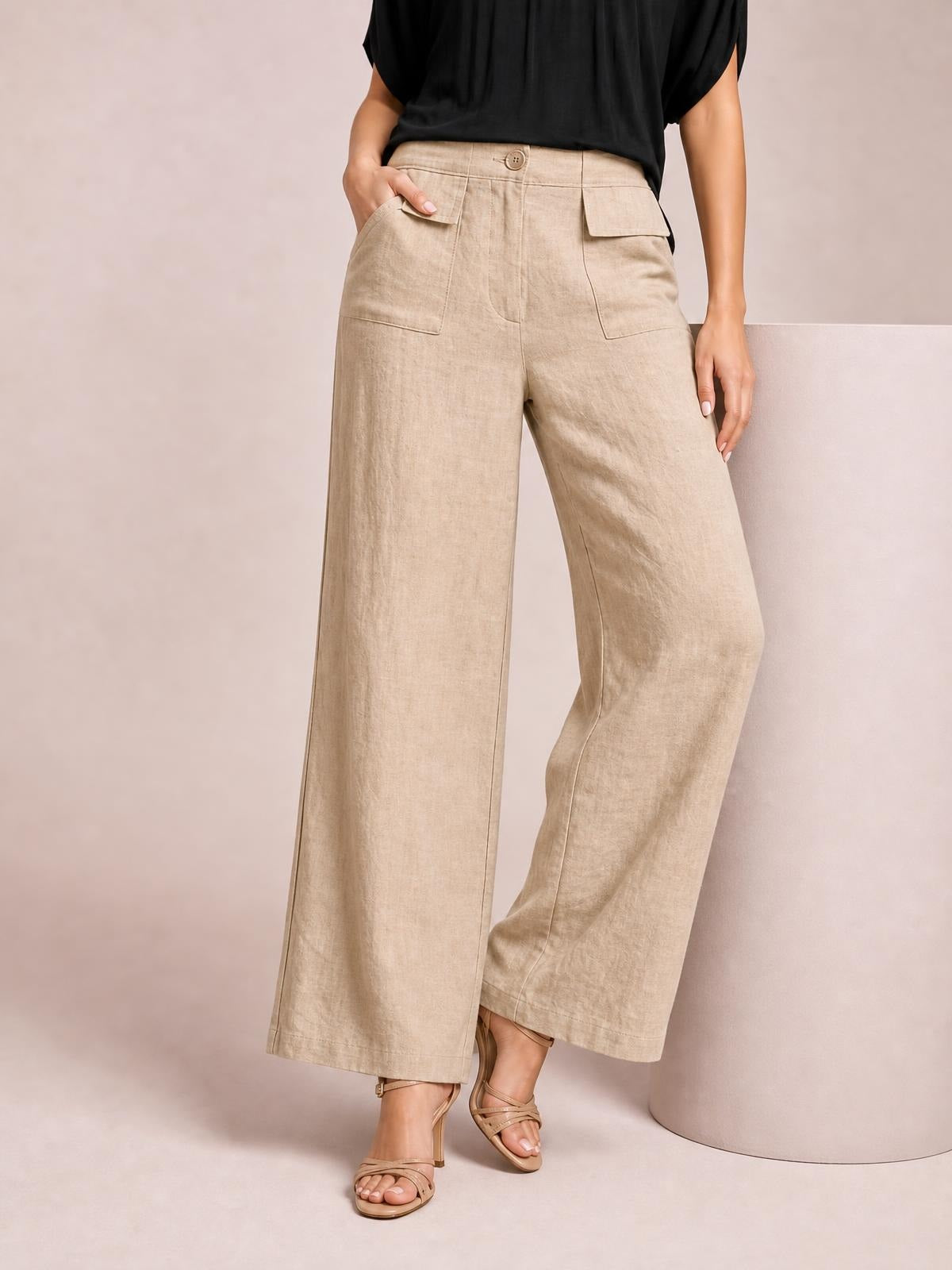Model wearing beige wide-leg pants with a high waist, button closure, front flap pockets, and a relaxed full-length silhouette.