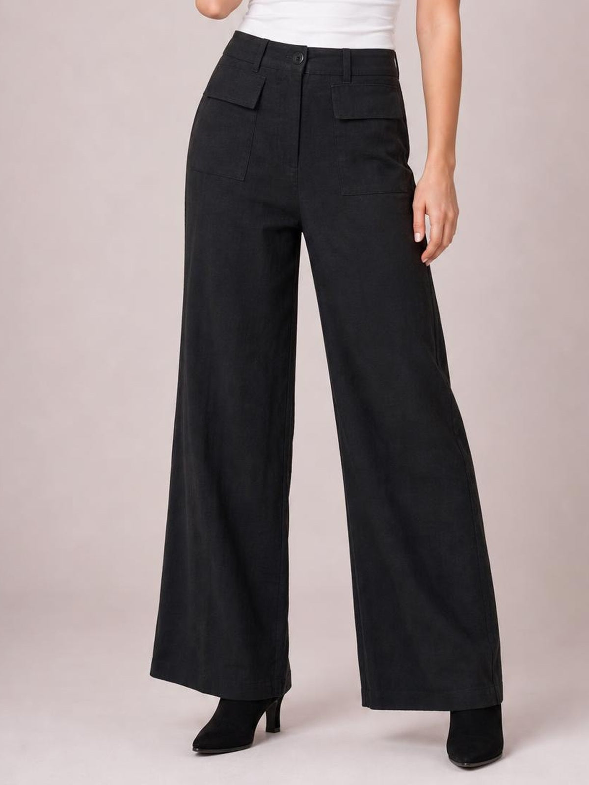 A standing model wears black wide-leg pants with a structured waistband, belt loops, button closure, and multiple visible patch pockets.