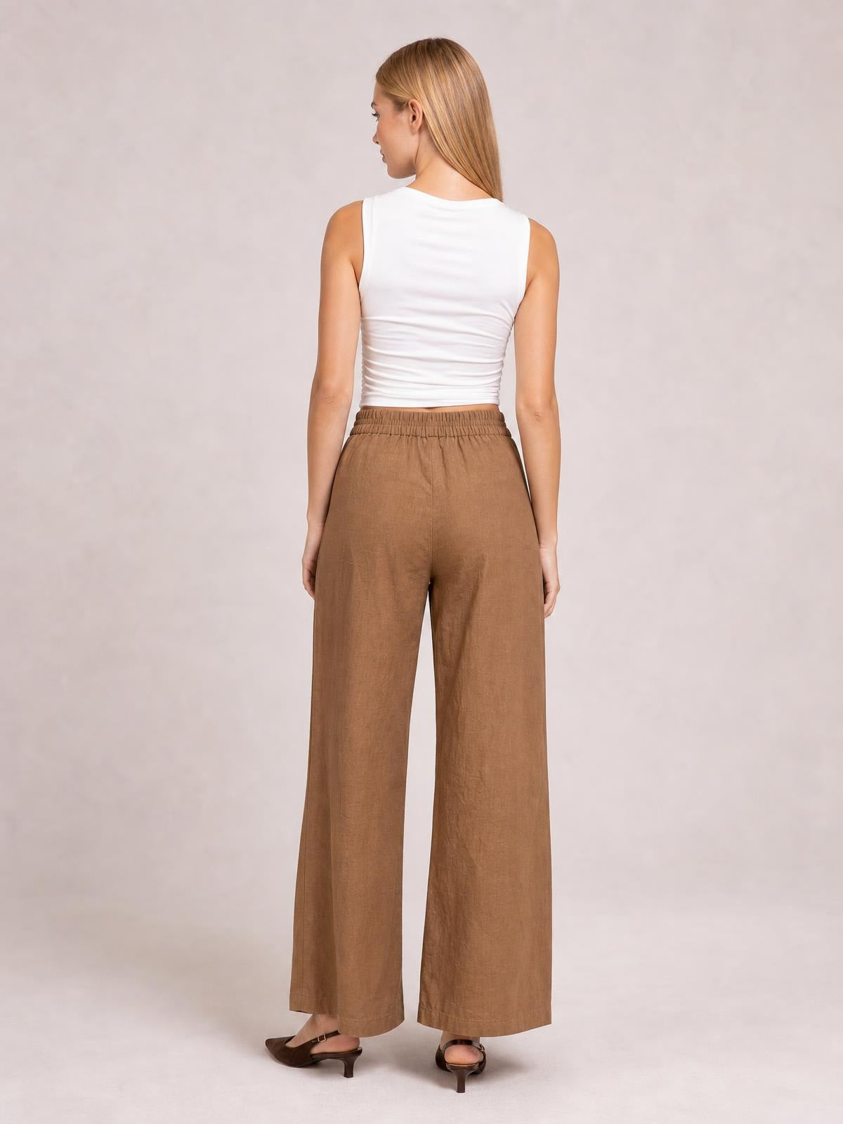 Model shown from the back wearing brown wide leg pants with an elasticized waistband, relaxed full-length silhouette, and side pockets.
