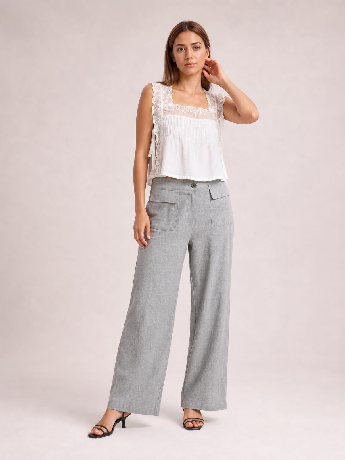 Model stands in gray wide leg pants with a relaxed silhouette, button closure, and large flap pockets, styled with a white top and black sandals.