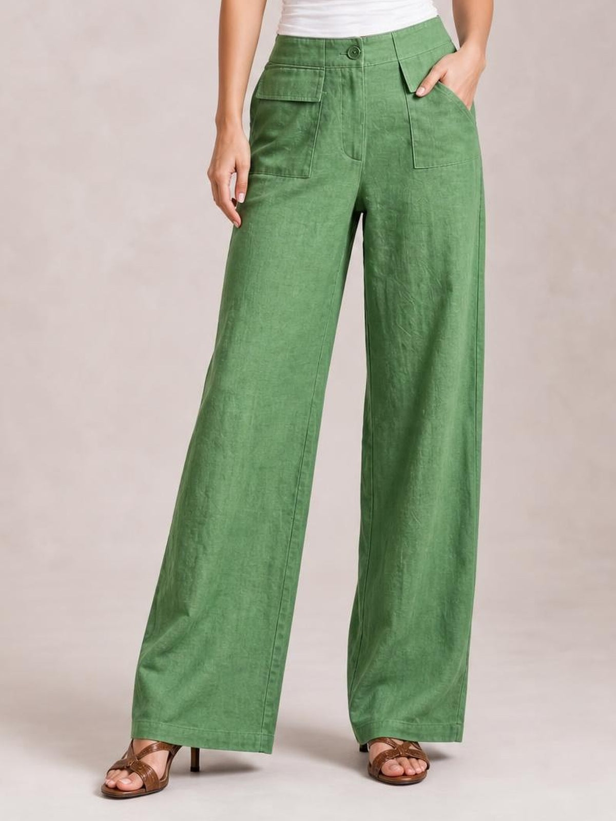 Model wearing green wide leg pants with a high waist, button closure, front patch pockets, and straight, flowing legs, with one hand in a pocket.