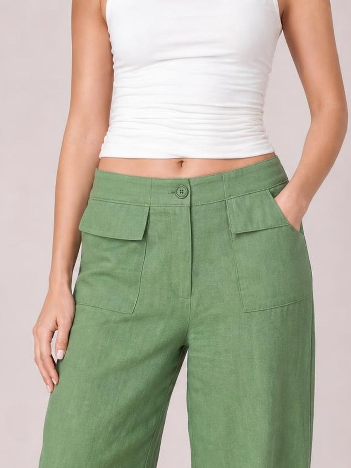 Model wears green wide leg pants with a button closure, belt loops, front patch pockets, and a relaxed silhouette, with one hand in a pocket.