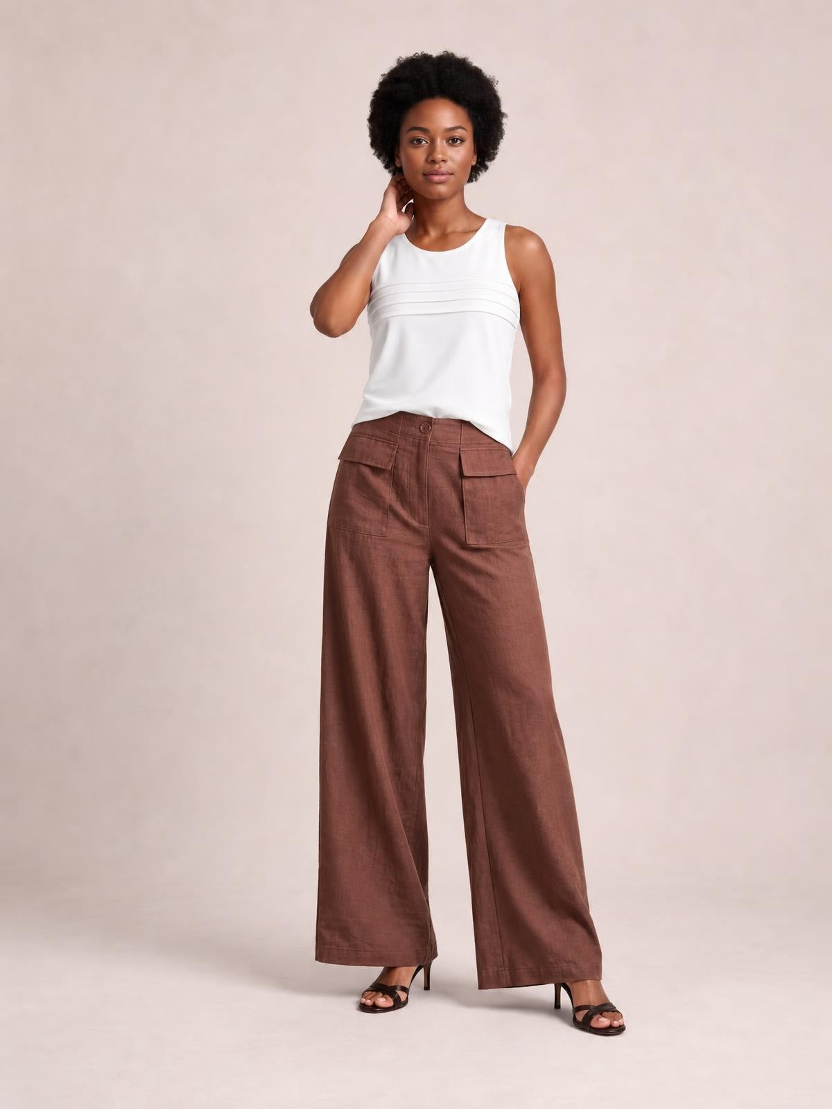 Model poses in brown wide leg pants with a high waist, button closure, stitched front panels, and large flap pockets.