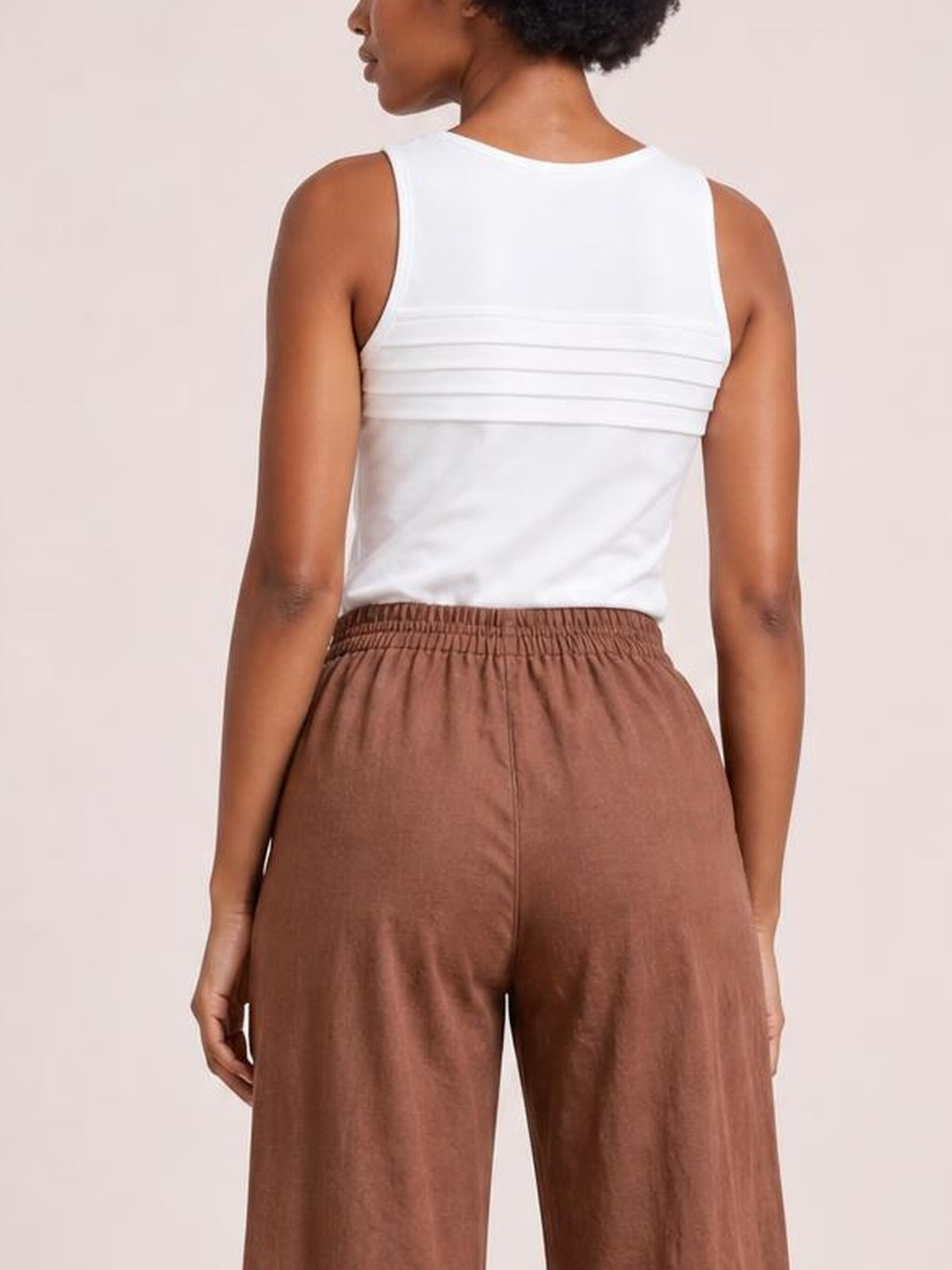 A model stands in a back view wearing brown wide leg pants with a gathered elastic waistband, relaxed silhouette, and smooth flowing construction.
