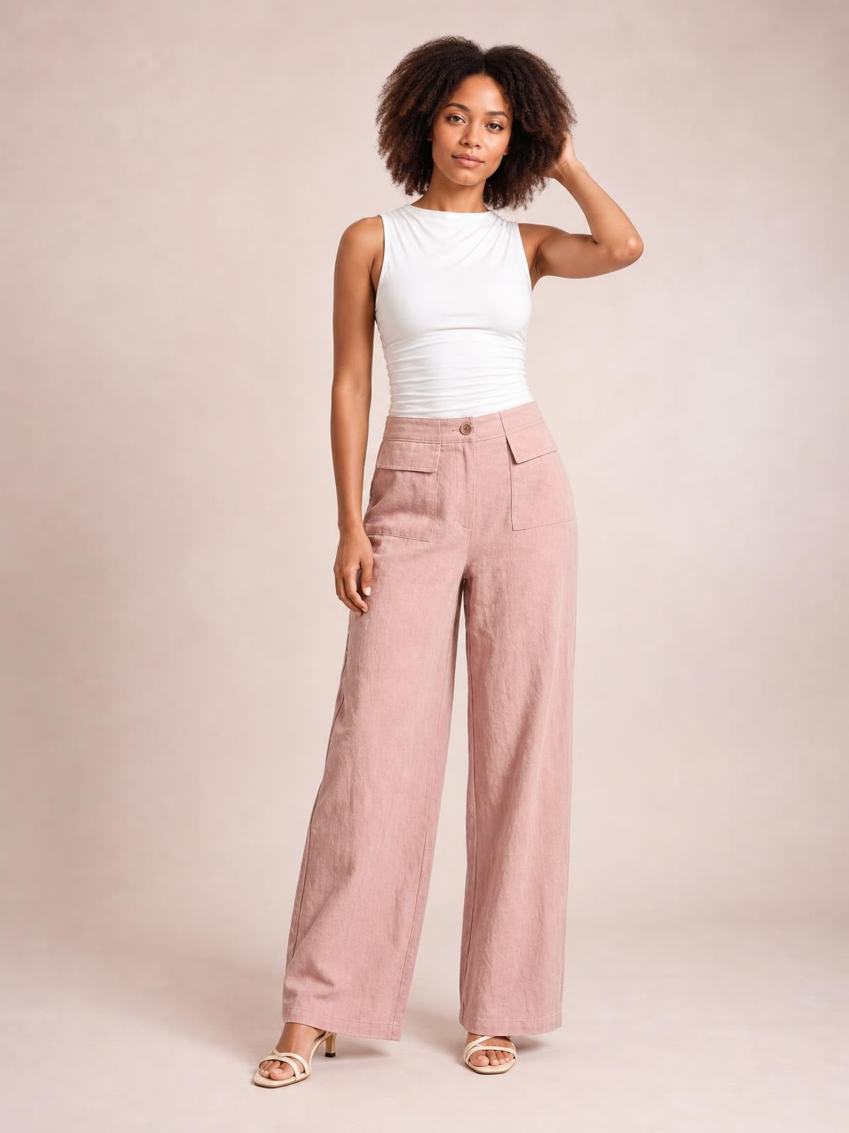 Model poses in pink wide leg pants with a button closure, belt loops, and large front patch pockets, styled with a white sleeveless top.
