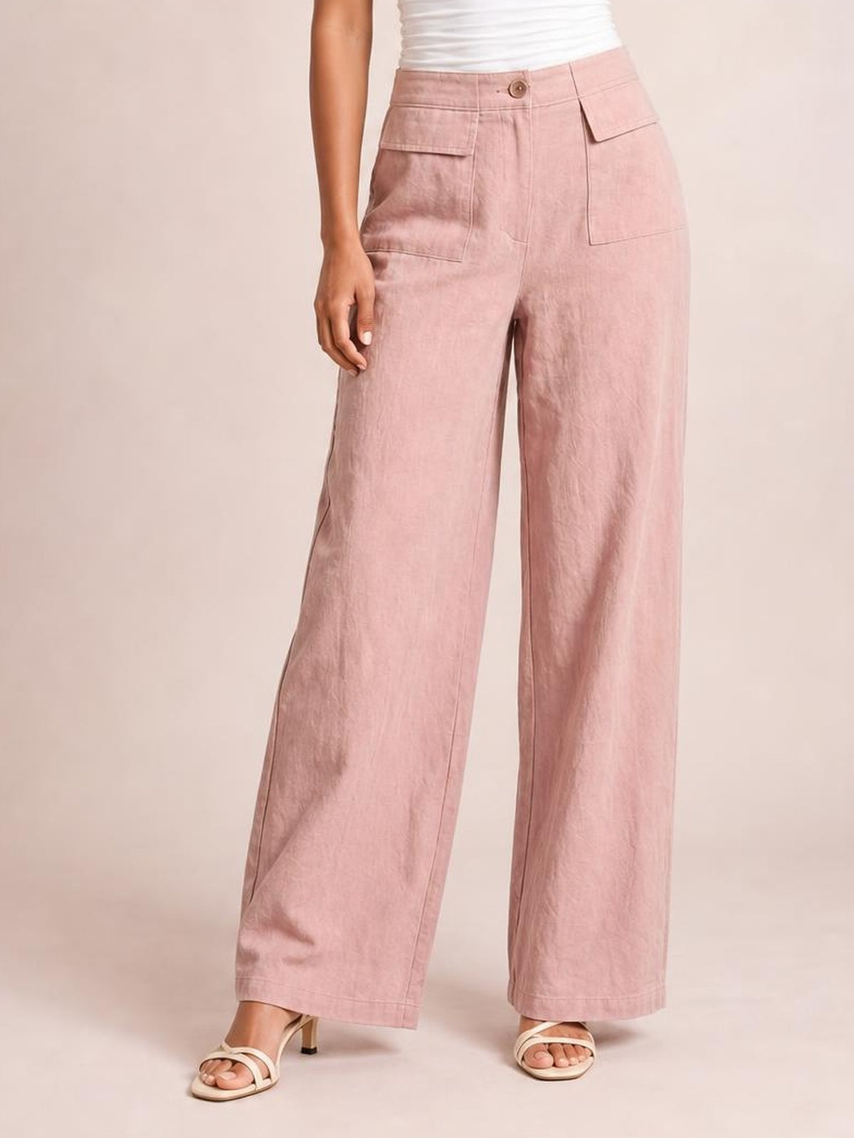 Model poses in pink wide leg pants with a buttoned waistband, large patch pockets, visible stitching, and a relaxed full-length silhouette.