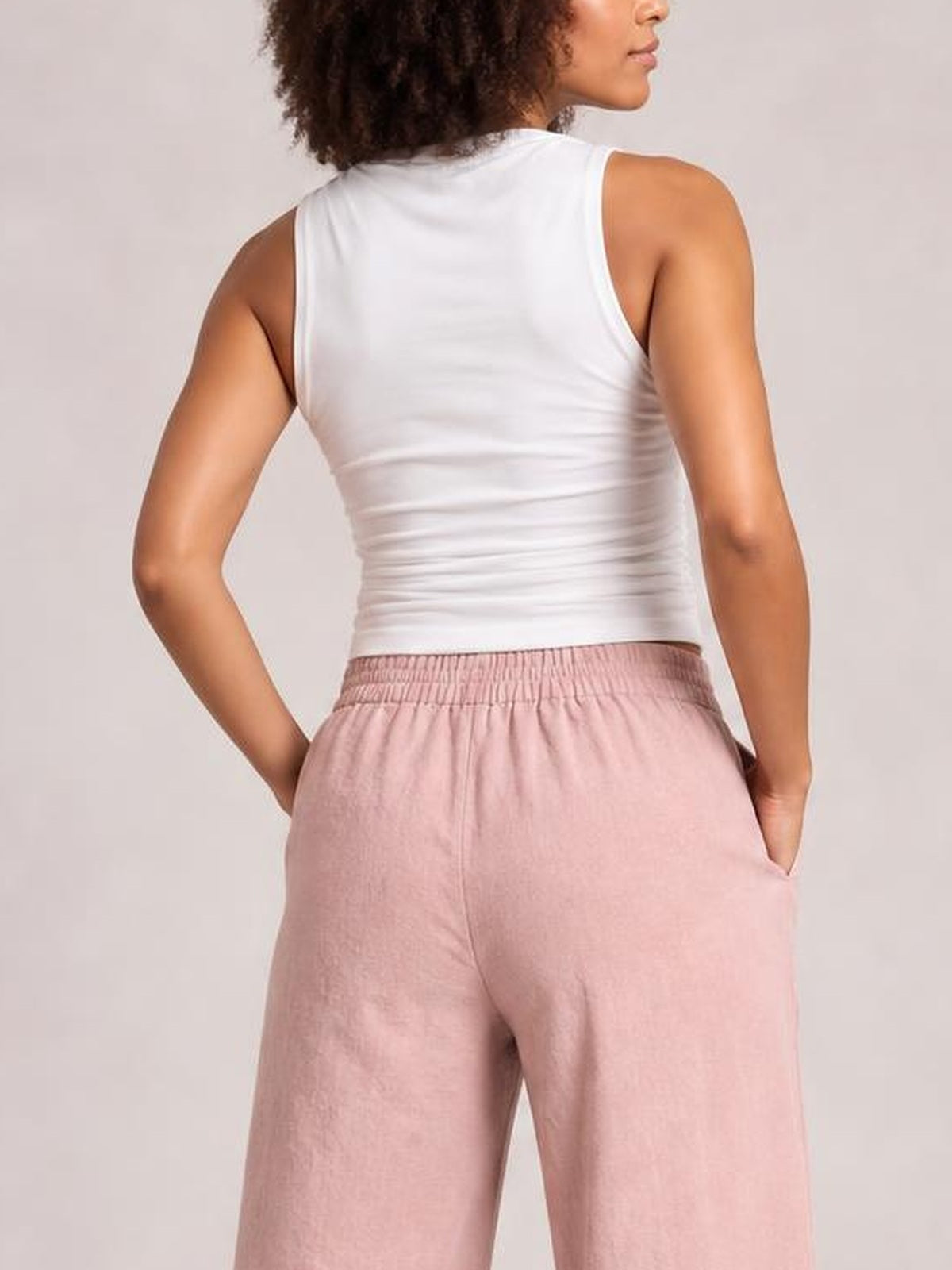Model viewed from behind wears pink wide leg pants with an elastic waistband and side pockets, standing with both hands tucked into the pockets.