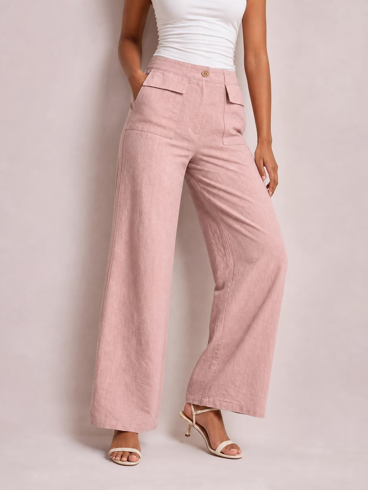 Model wearing pink wide leg pants with a high-rise button waist, stitched seams, and flap-style front pockets, posed with one hand in a pocket.
