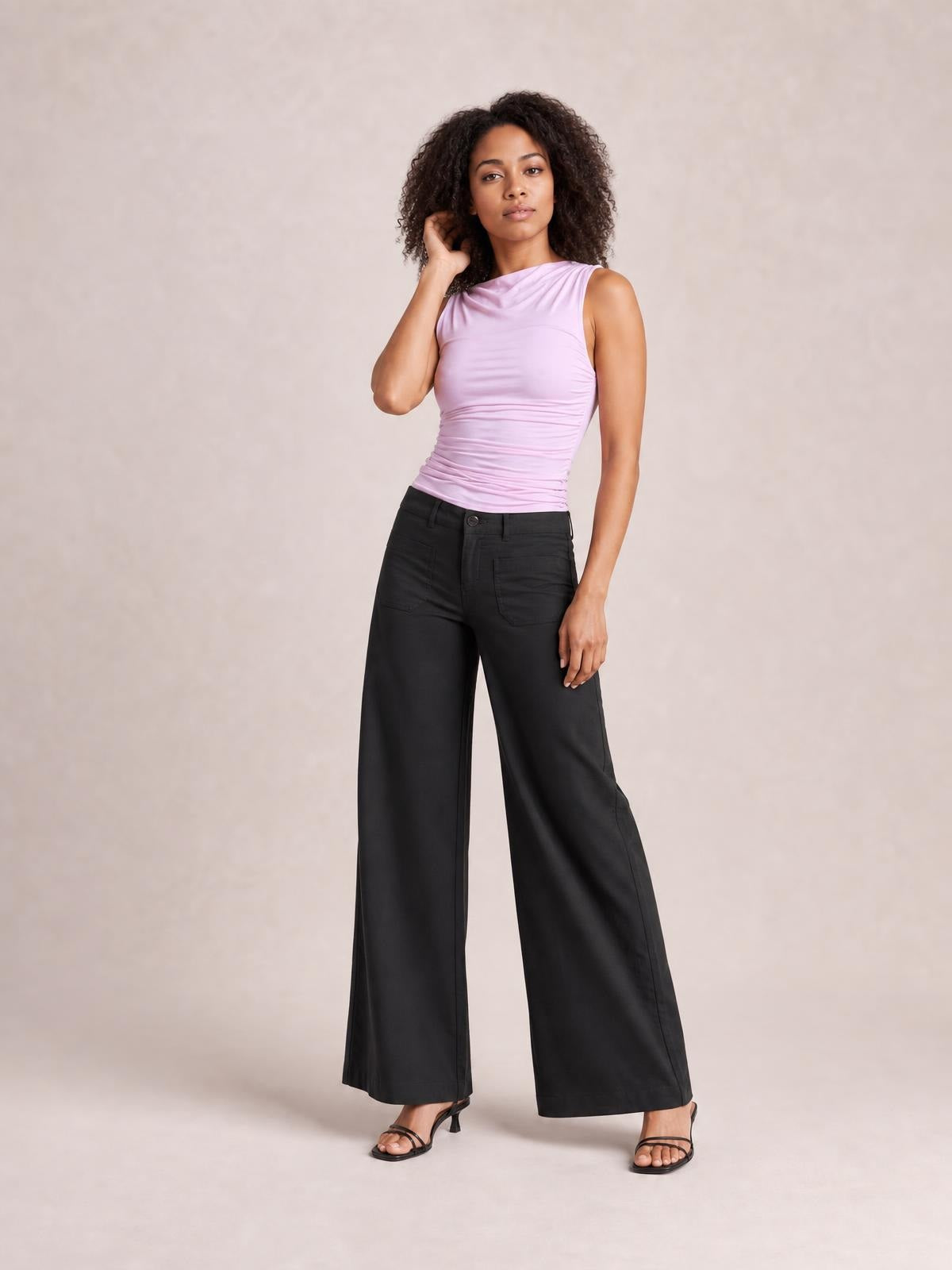 Model poses in black wide leg pants with front pockets, a button closure, belt loops, and a full-length relaxed silhouette.