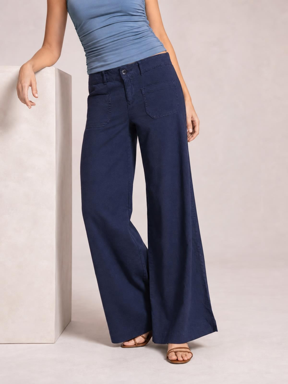 A model wears navy wide leg pants with a structured waistband, button fly, and large front patch pockets while standing in a relaxed pose.