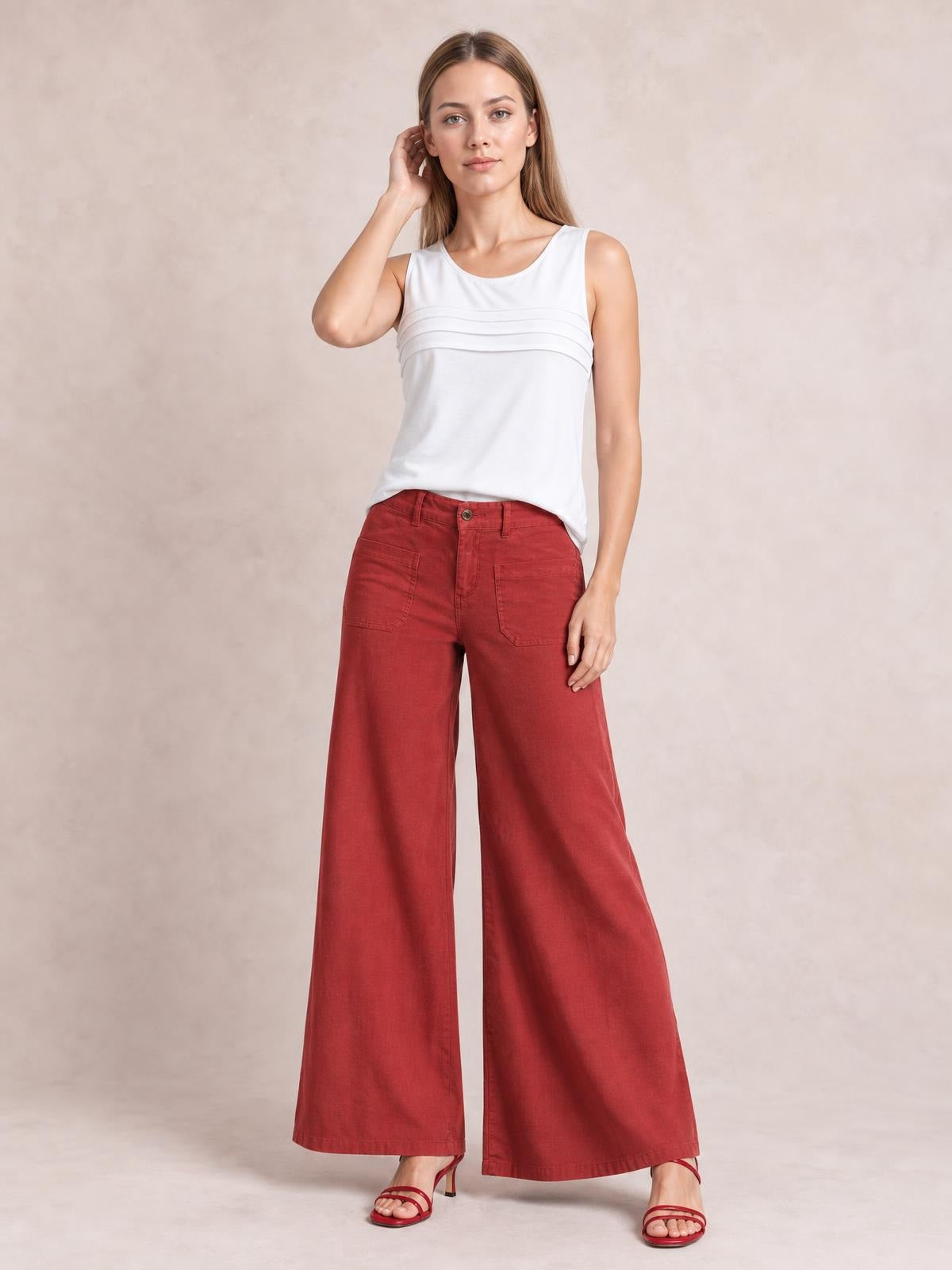 Model wearing red wide leg pants with front pockets, belt loops, and a button closure, posed standing in sandals with one hand near her hair.