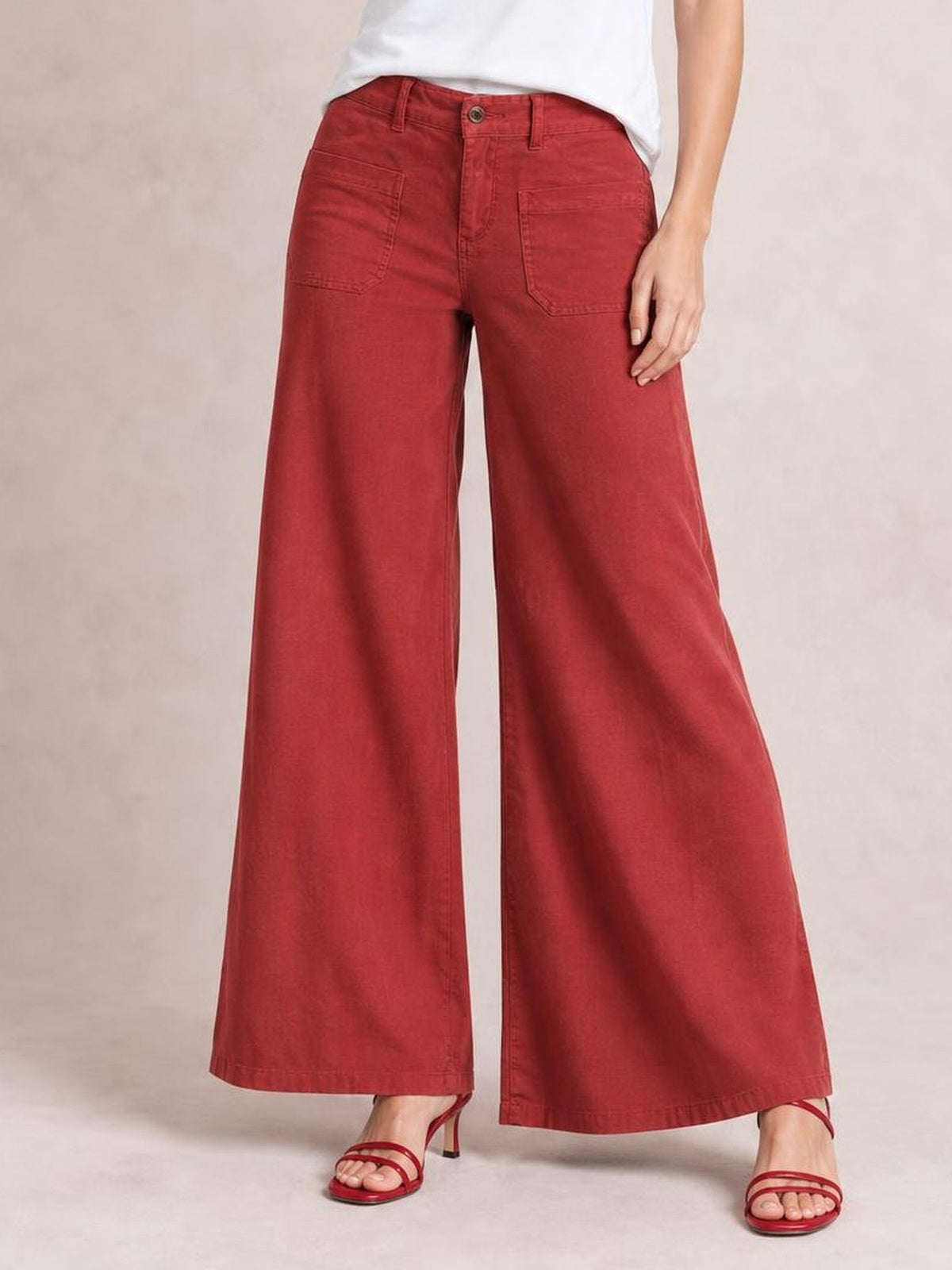 Model wearing red wide-leg pants with front pockets, belt loops, button closure, and full-length legs, posed with one hand resting on the hip.