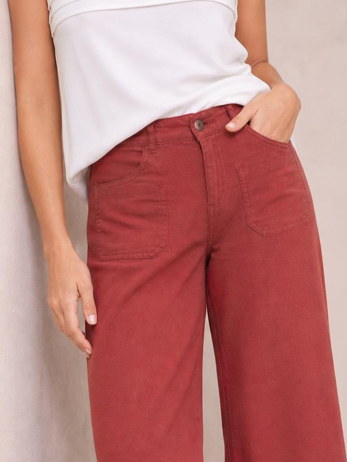 Model wearing brick-red wide leg pants with a button closure, visible front patch pockets, and a relaxed straight silhouette.