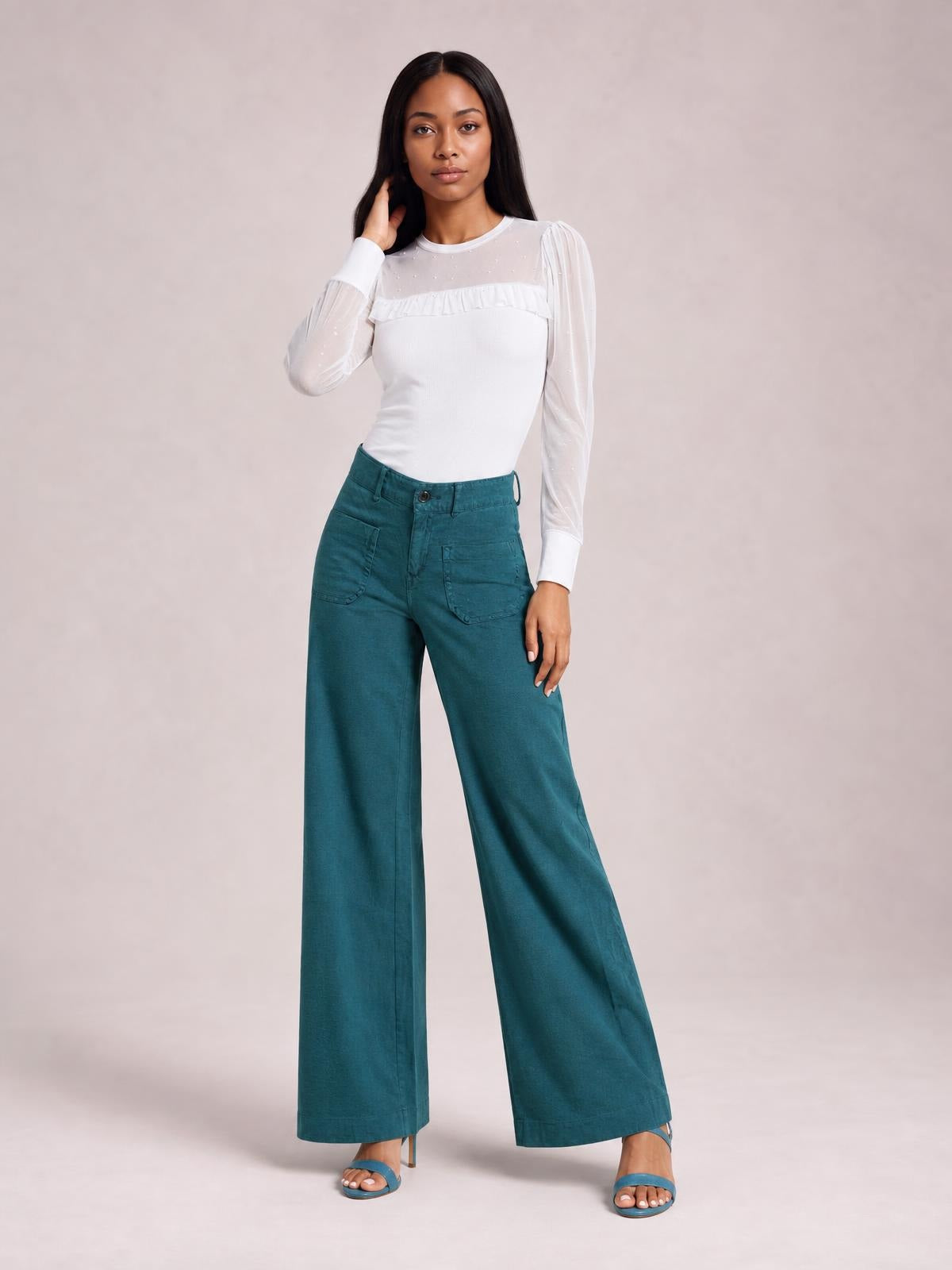 Model standing in teal wide-leg pants with front patch pockets, a button closure, belt loops, and a full-length relaxed silhouette.