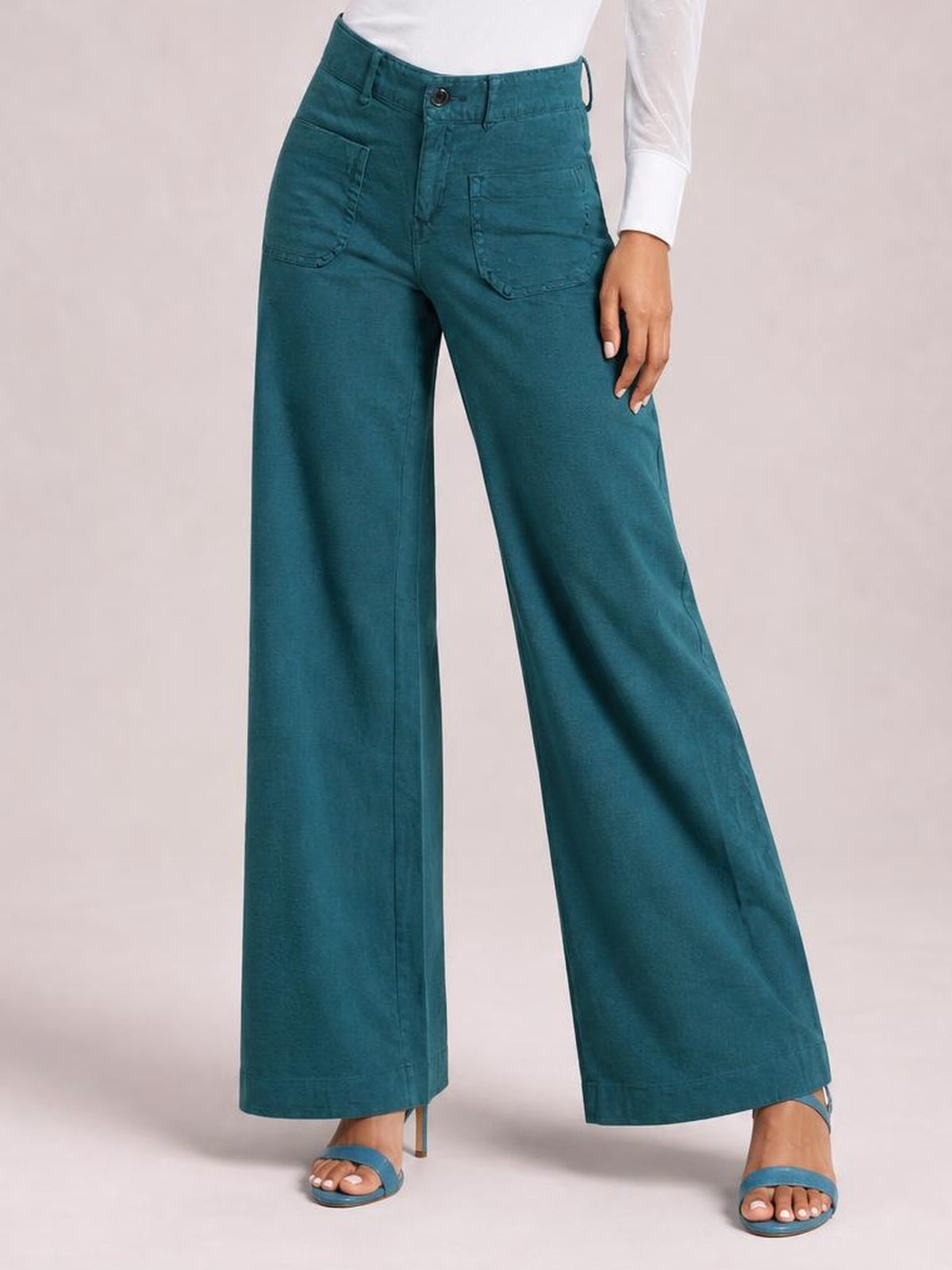 A model wears teal wide leg pants with front pockets, belt loops, button closure, stitched seams, and a full-length silhouette.