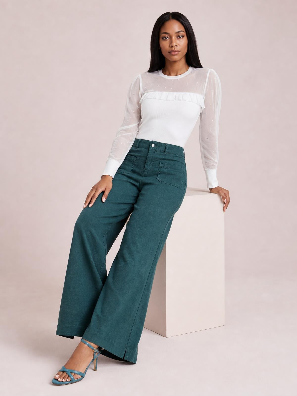 Model poses in teal wide-leg pants with front and side pockets, a button closure, belt loops, and a full-length relaxed silhouette.