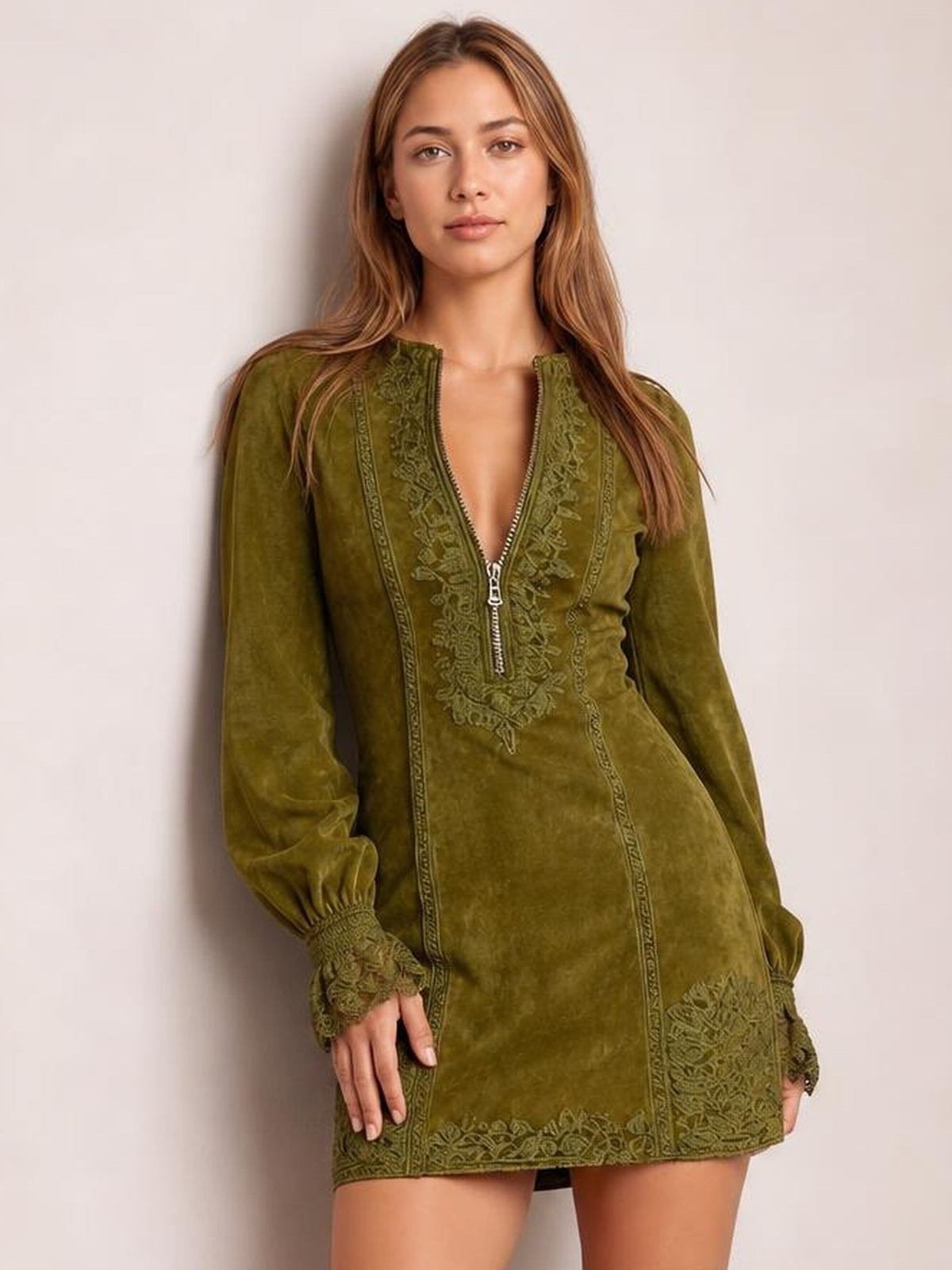 A model wears an olive green long-sleeve mini dress with a front zipper, fitted silhouette, lace-trimmed neckline, cuffs, and hem.