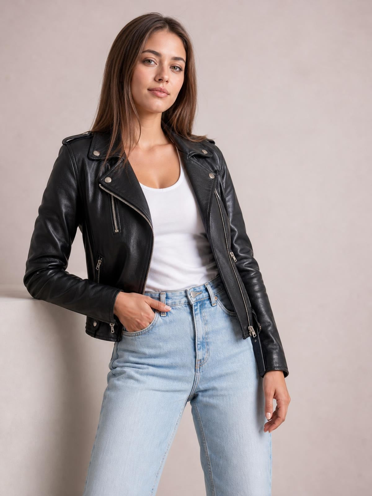 A model wears a black leather-look motorcycle biker jacket with an open asymmetrical zip front, wide lapels, snap details, zip pockets, and a fitted silhouette.