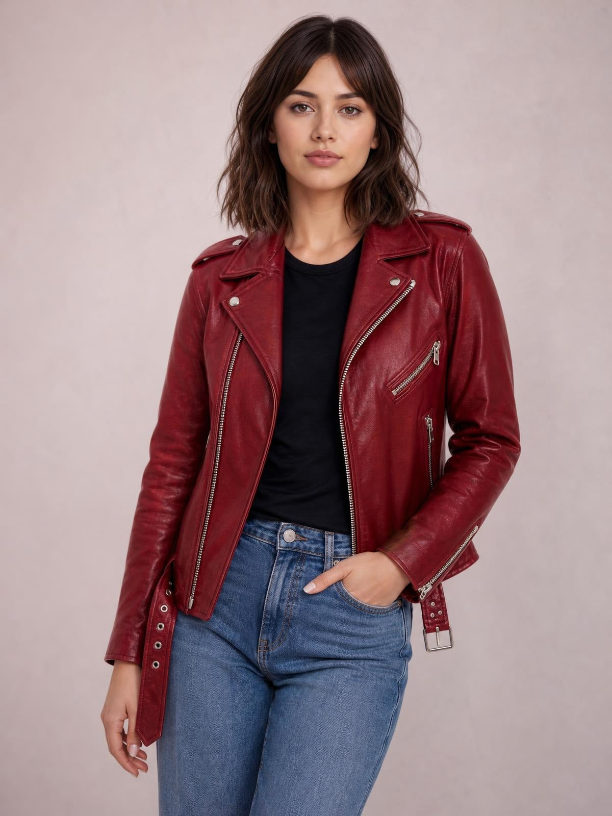 A model wears a burgundy leather motorcycle biker jacket with an asymmetric zip, wide lapels, shoulder epaulettes, zip pockets, and a belted hem.