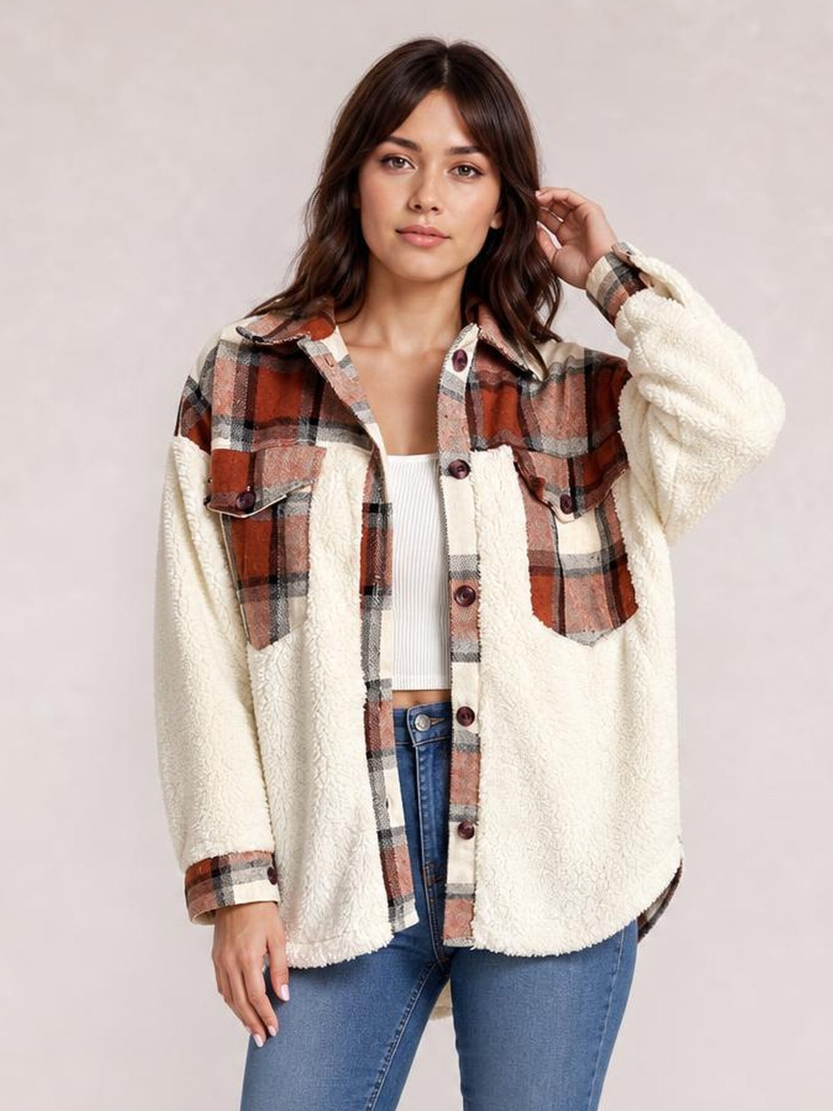 Model poses in a relaxed fuzzy button-up jacket with cream sherpa panels, rust plaid accents, long sleeves, chest pockets, and a loose silhouette.