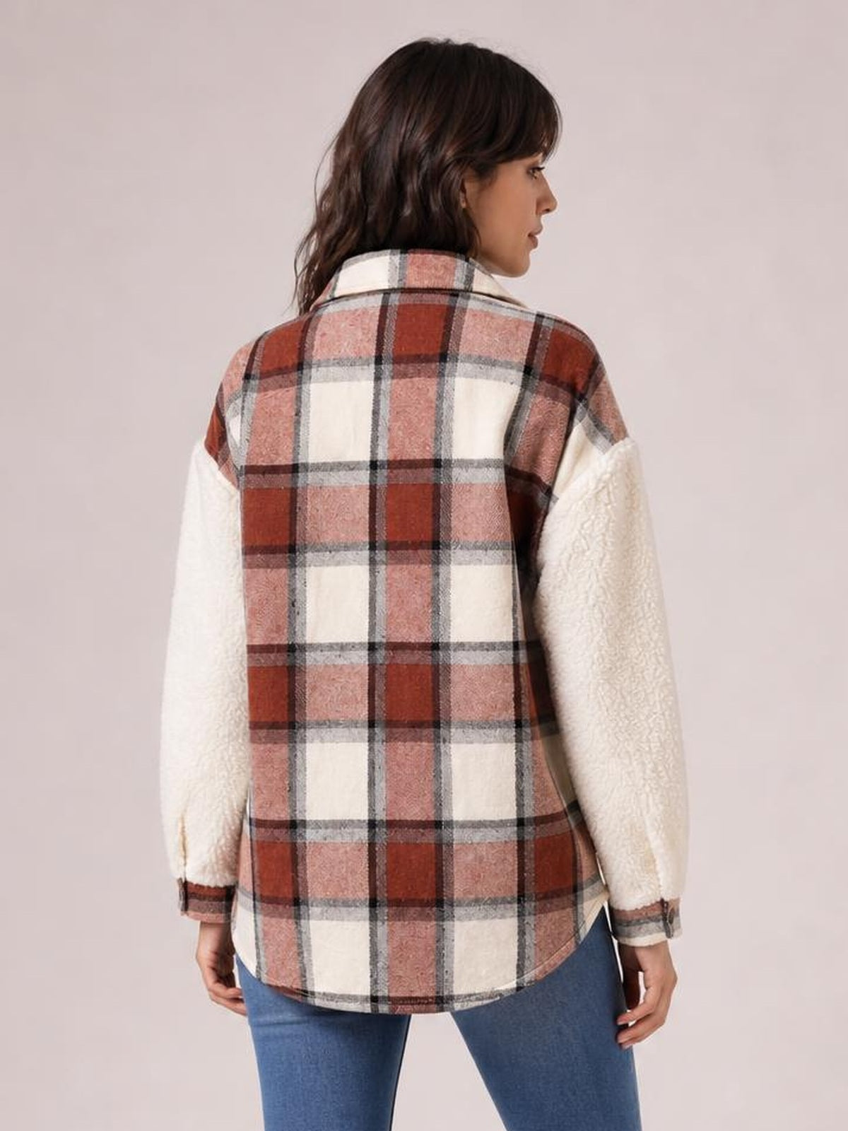 A model shows the back of a fuzzy button-up long sleeve jacket with a red, pink, cream, and gray plaid body, cream textured sleeves, and a relaxed curved-hem silhouette.