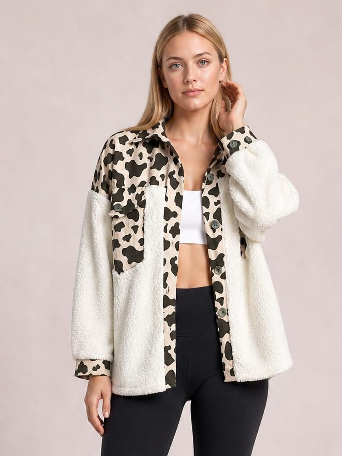 Model wearing a thick fuzzy button-up jacket with cow-print panels, white sherpa sleeves and front pockets, long sleeves, and a relaxed silhouette.