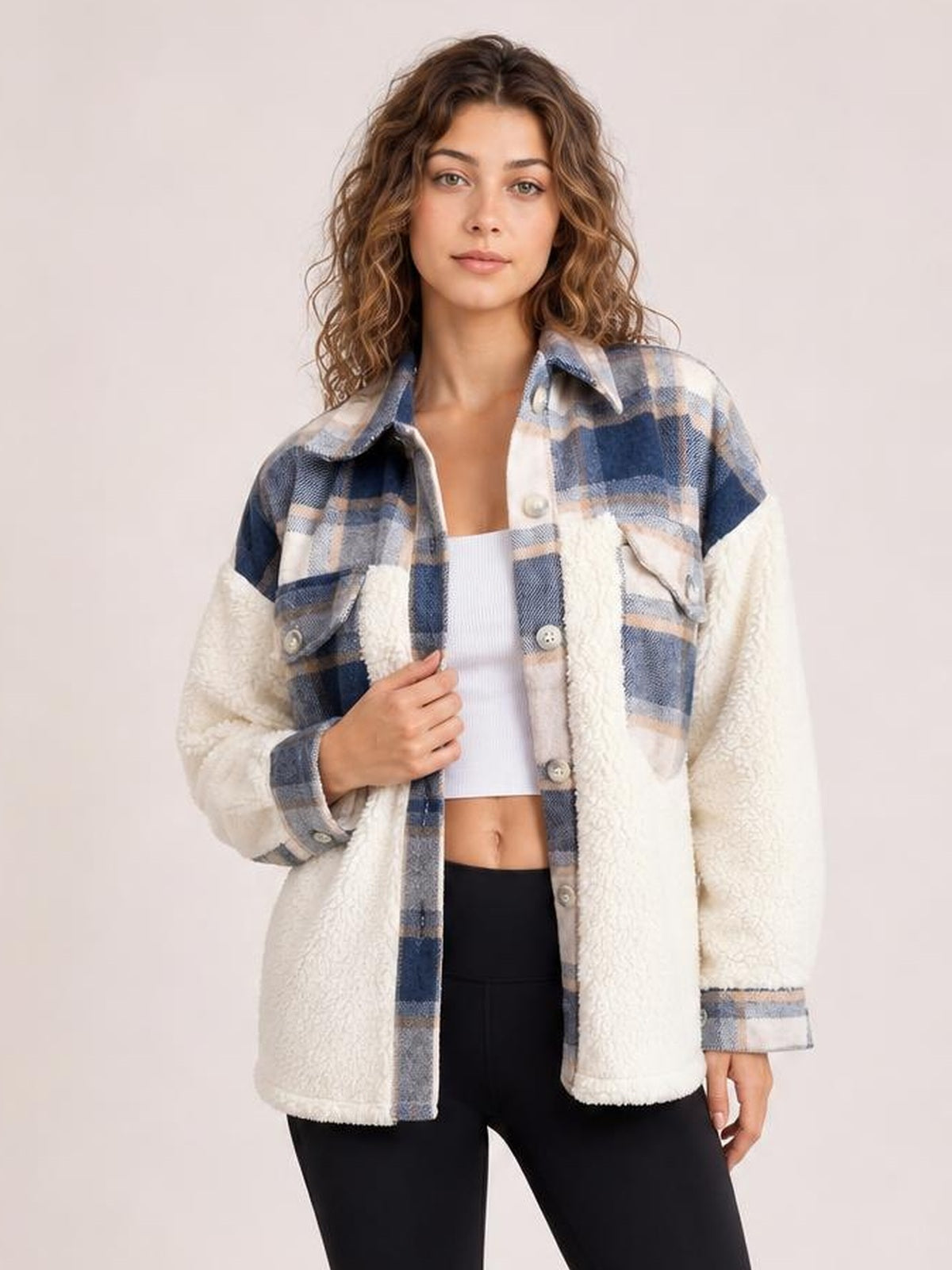 Model poses in a fuzzy blue-and-cream plaid button-up long sleeve jacket with sherpa panels, flap pockets, and a relaxed hip-length silhouette.