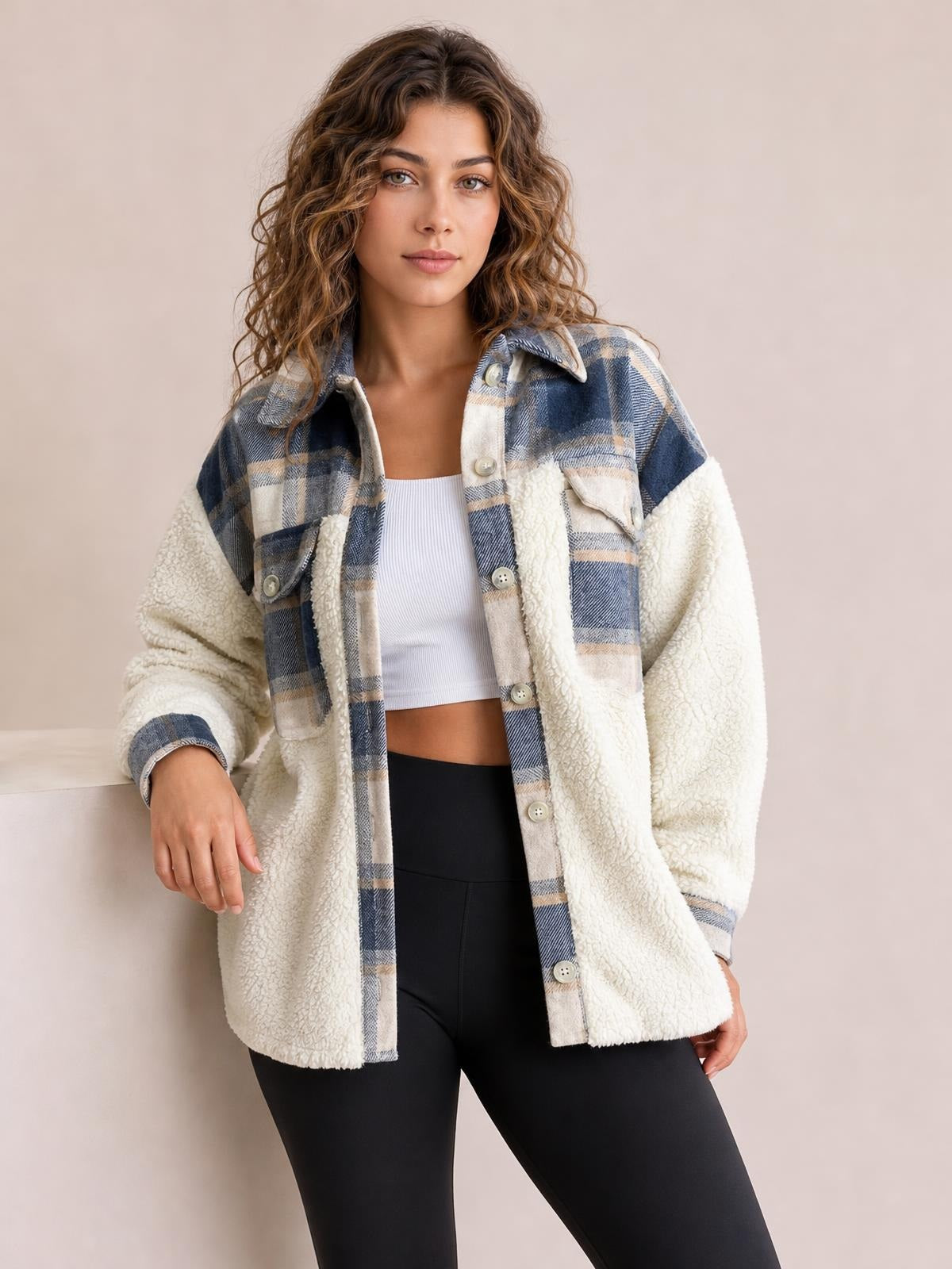 Model wears a thick fuzzy button-up jacket with cream sherpa sleeves, blue plaid panels, long sleeves, chest pockets, and a relaxed silhouette.